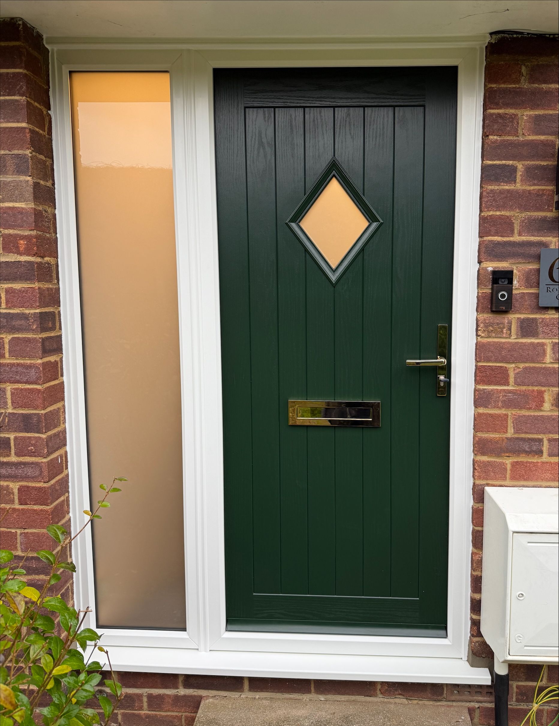 Green front door with diamond window and sidelight, set in brick.