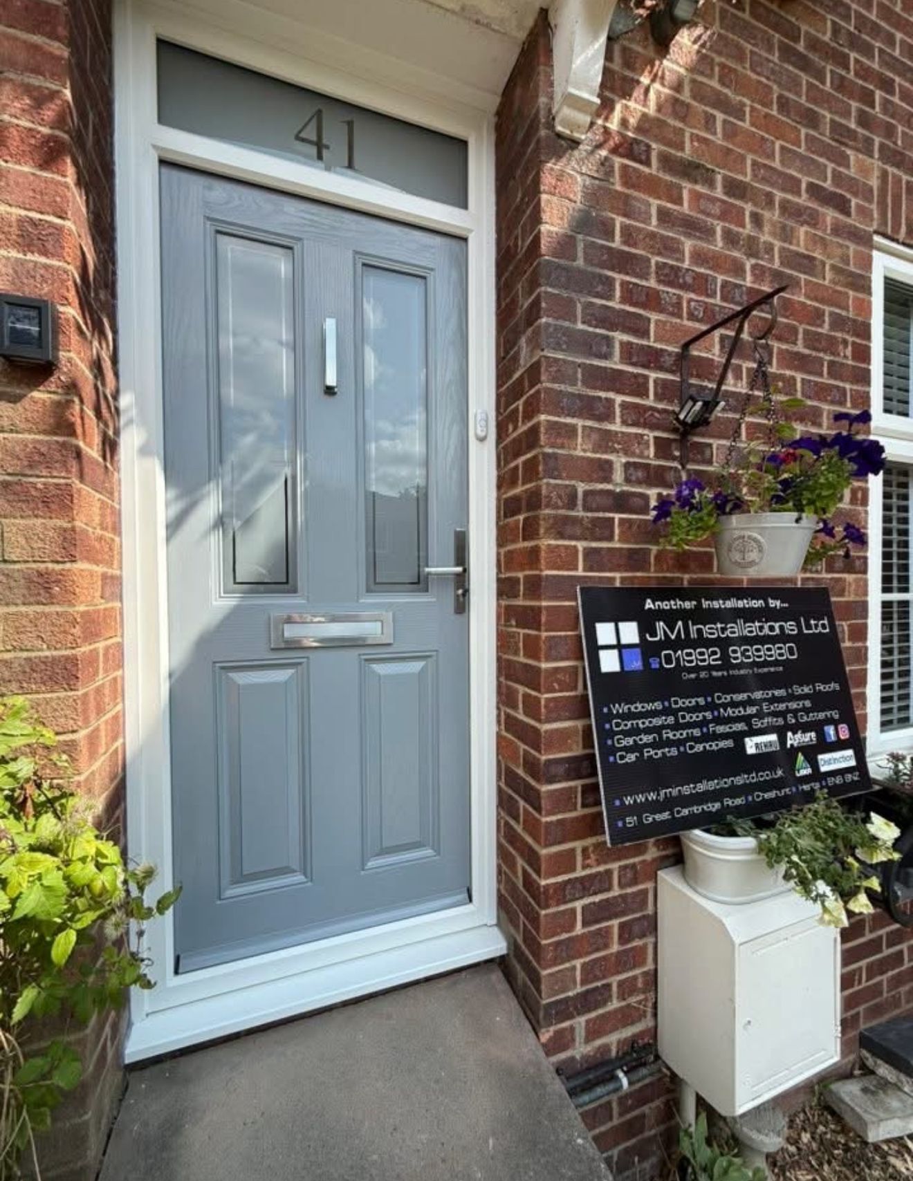 Grey front door with white trim, number 41 above, on a brick house. A sign to the side, plants.