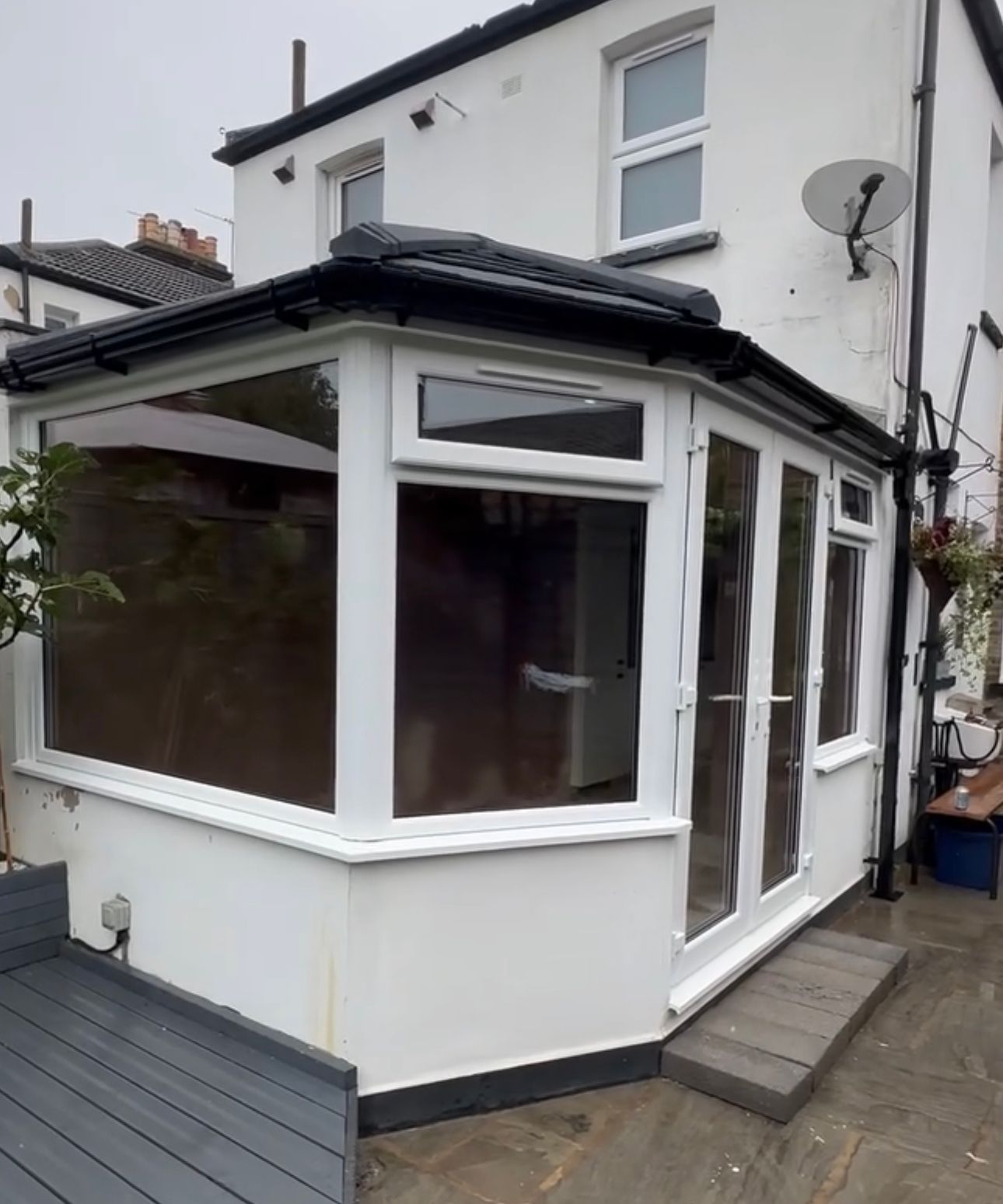 White sunroom addition to a house with large windows, dark roof, and a gray ramp.