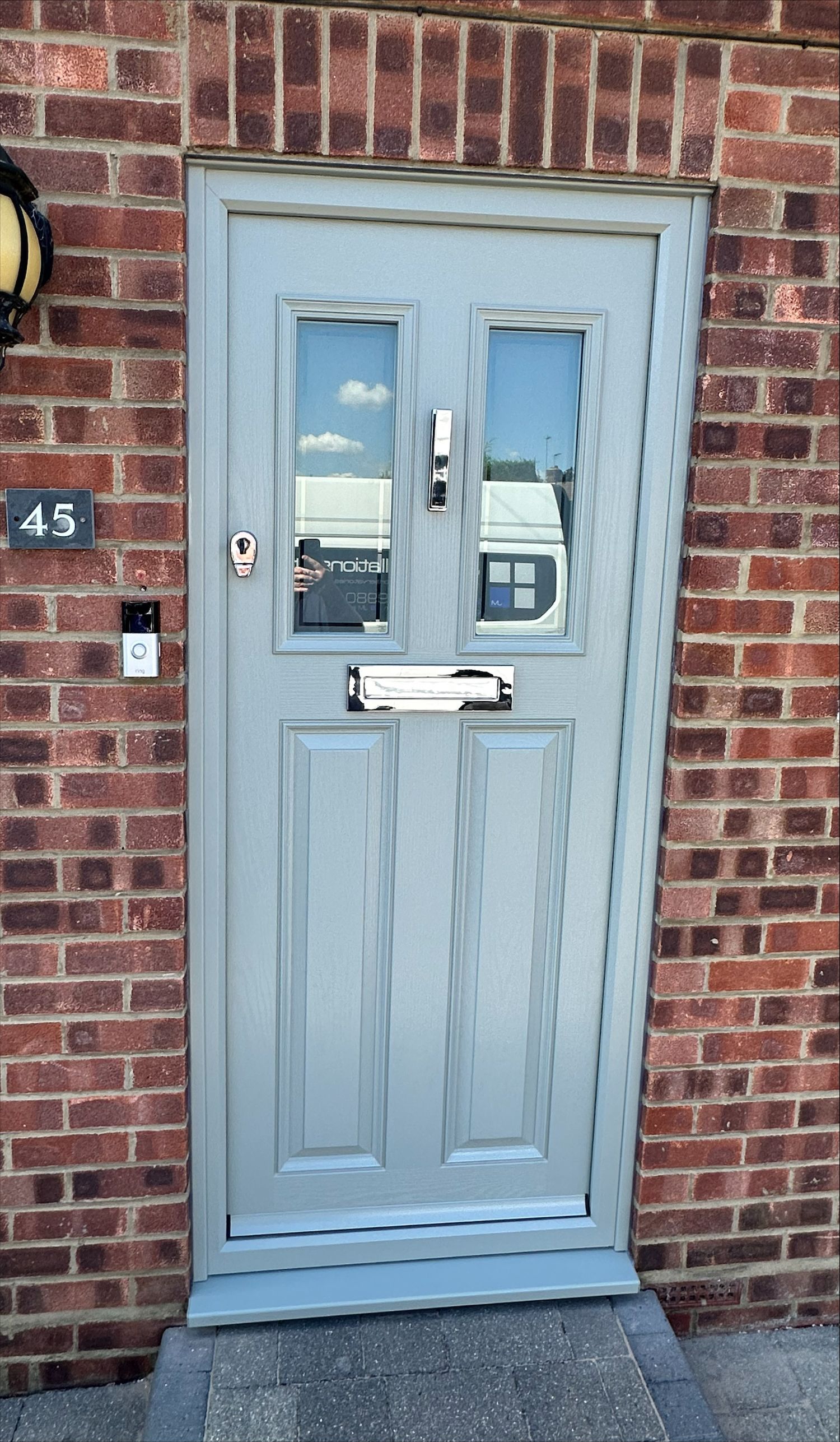 Grey front door with glass panels and brass hardware, set in a brick wall.
