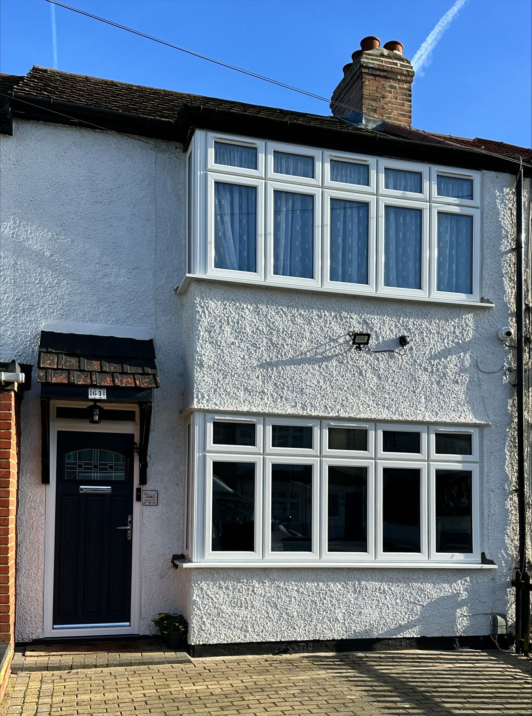 Two-story white house with bay windows, dark door, and brick pathway on a sunny day.