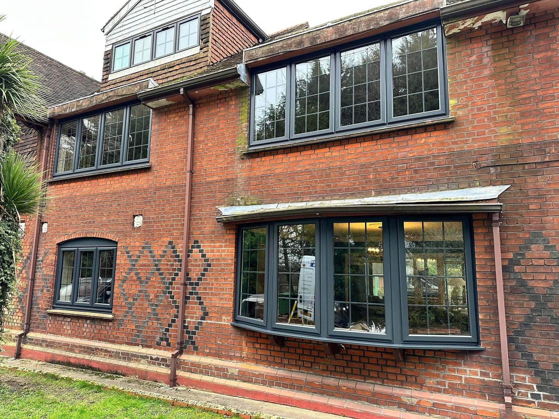 Red brick building with gray-framed windows, including a bay window, set under a tiled roof.