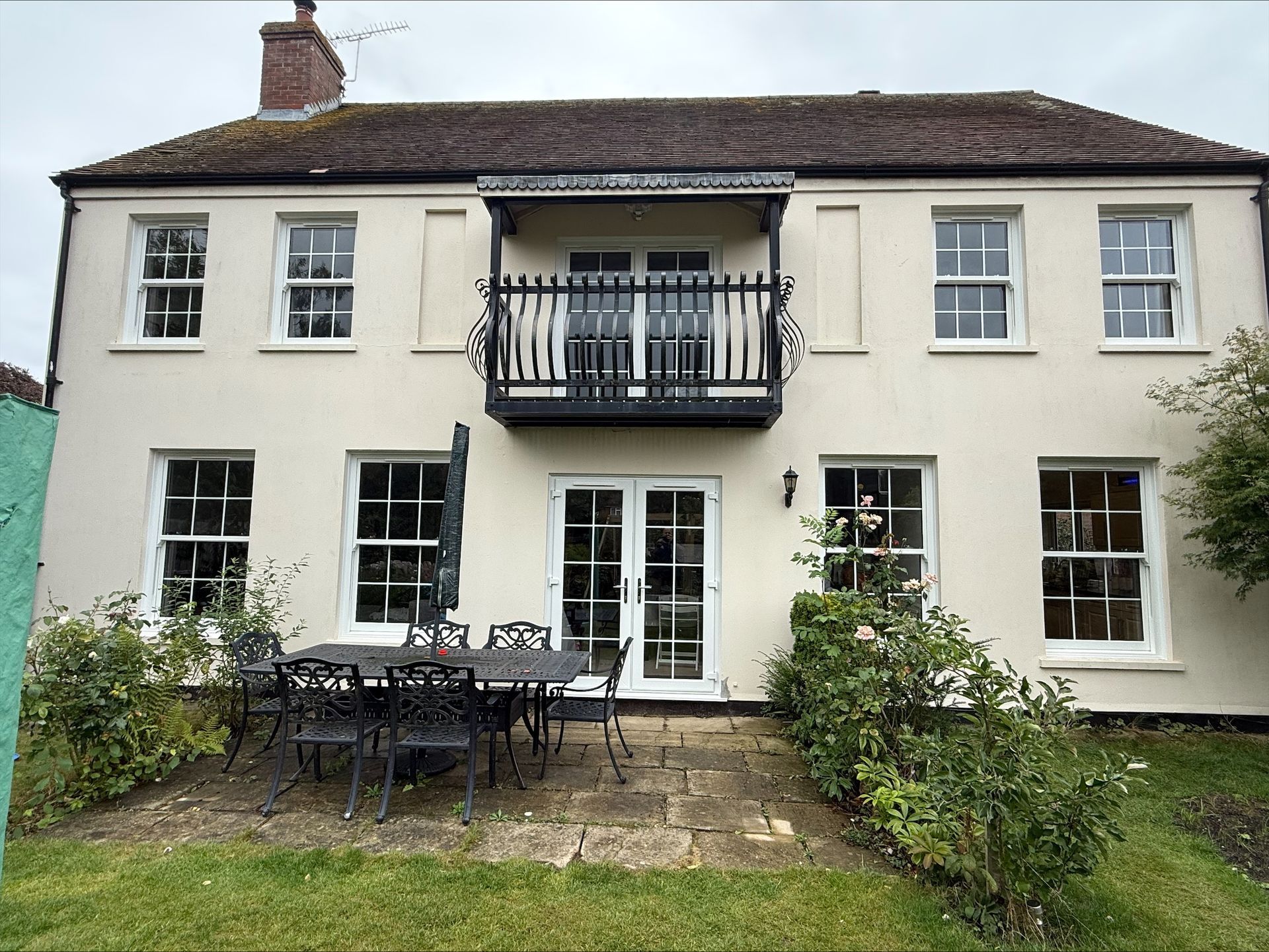 Beige house with white-framed windows, black balcony, and outdoor dining set on a lawn.