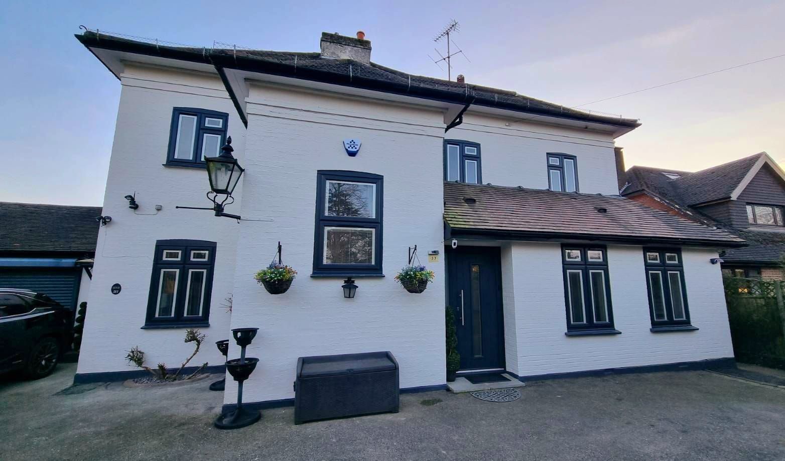 White two-story building with black trim, a dark door, and hanging flower baskets.