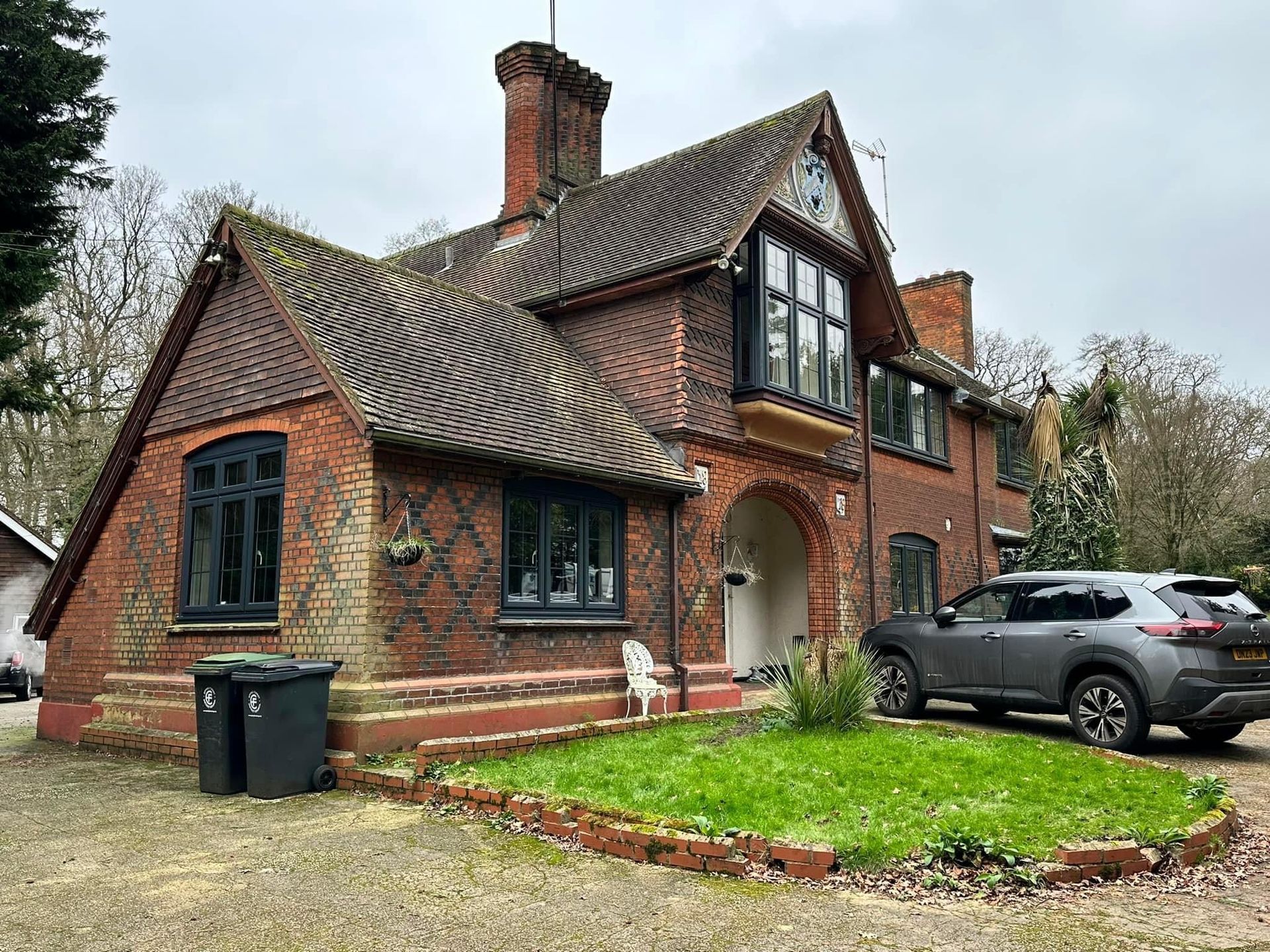 Brick house with gray SUV parked in front. Black windows and a small lawn.
