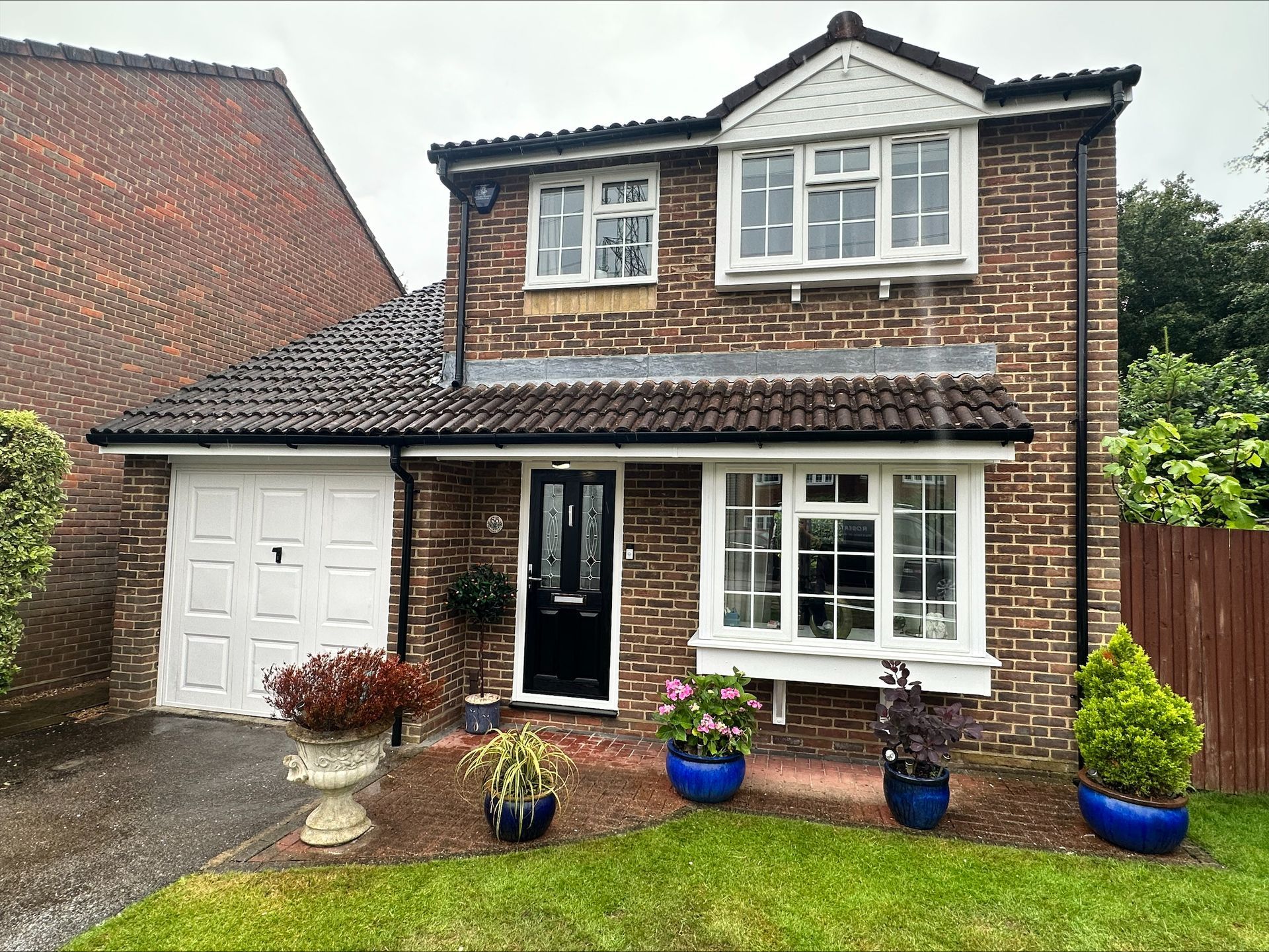Brick house with white trim, bay window, black door, and blue flower pots.