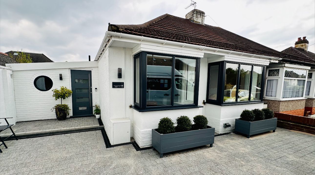 White bungalow with grey trim, window boxes, and a gravel driveway.