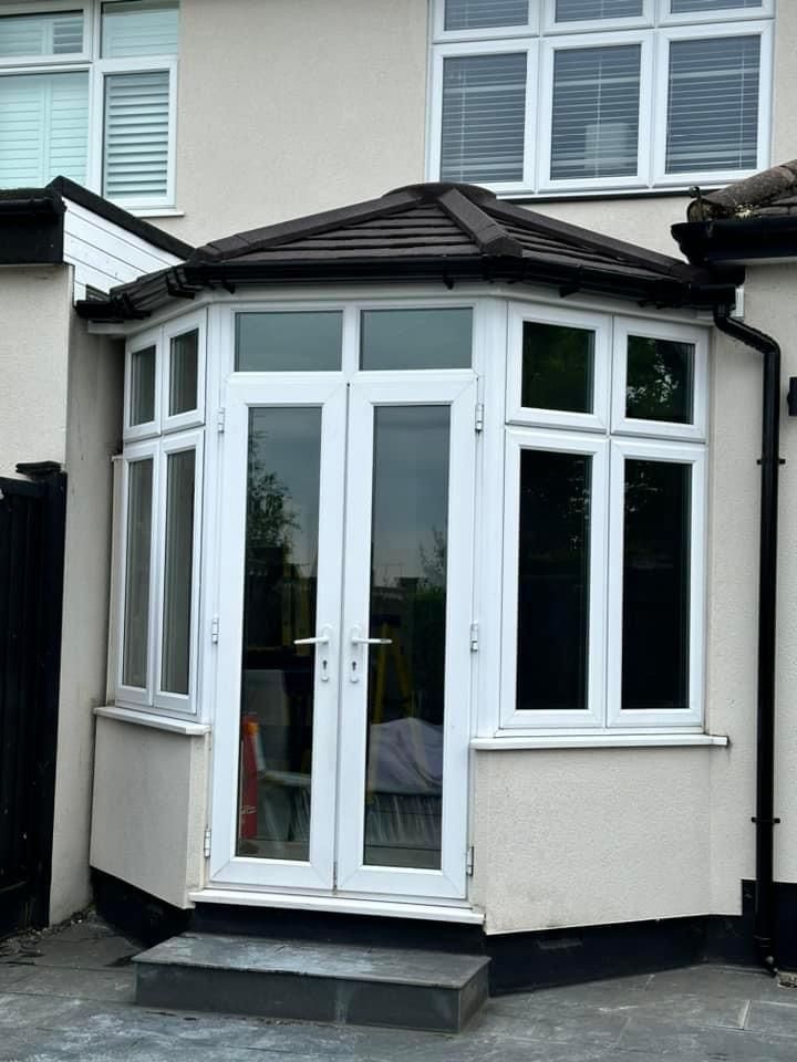 White-framed bay window with double doors, under a dark roof, two steps down from a house.