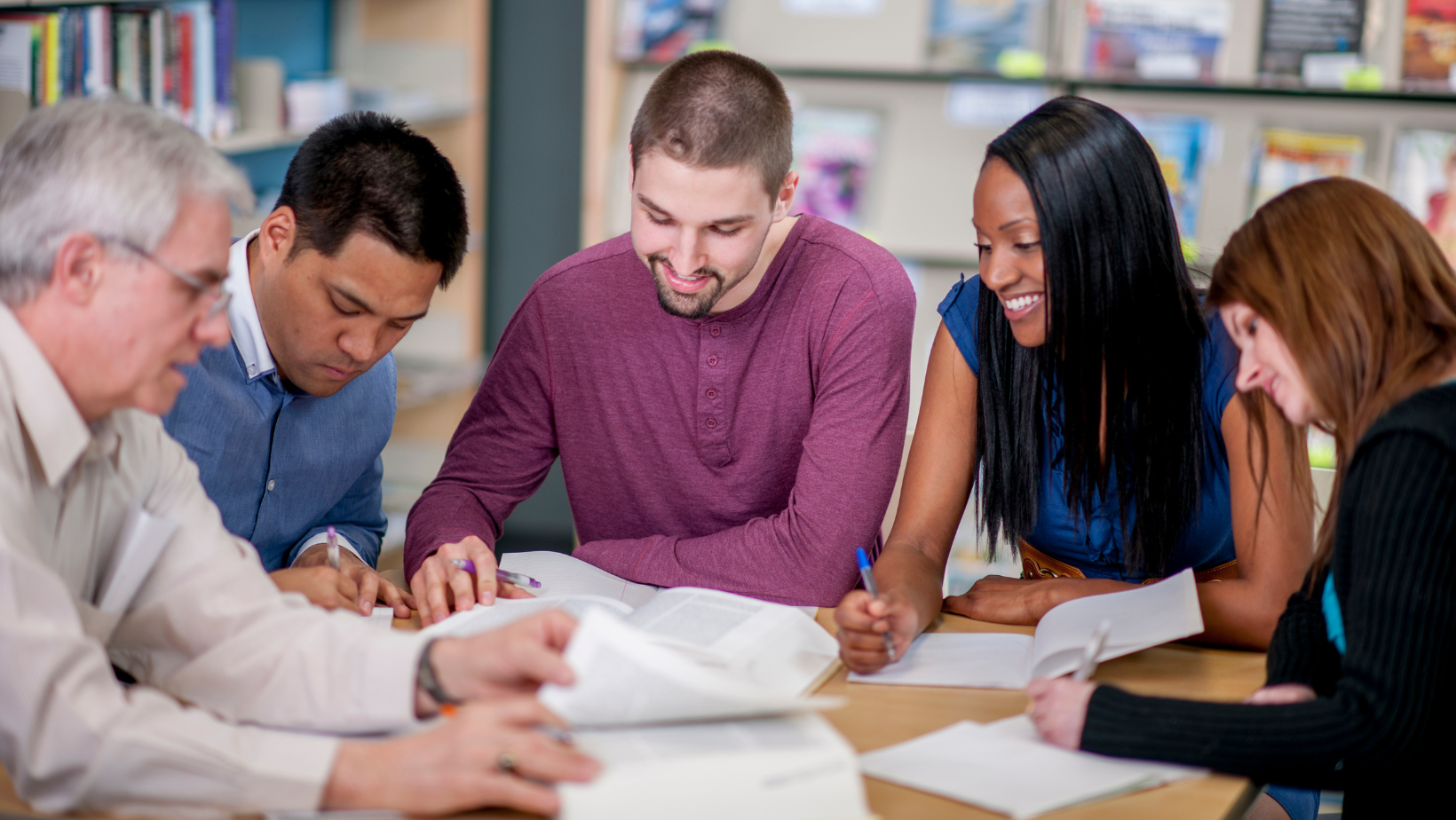 Small group of people collaborating around a table, reviewing papers and discussing together in a bright room