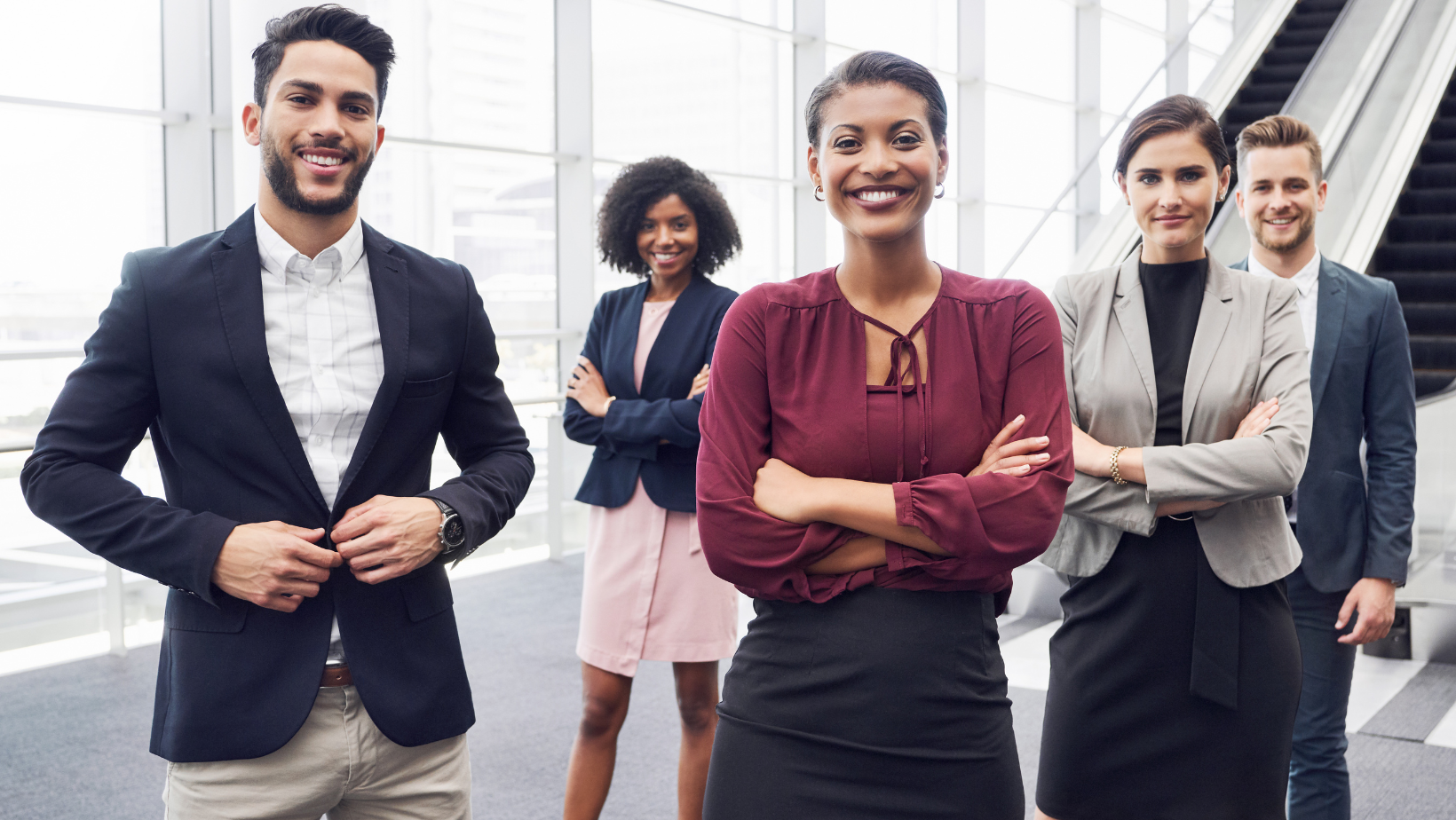 Four business professionals standing together in a bright office, smiling confidently.