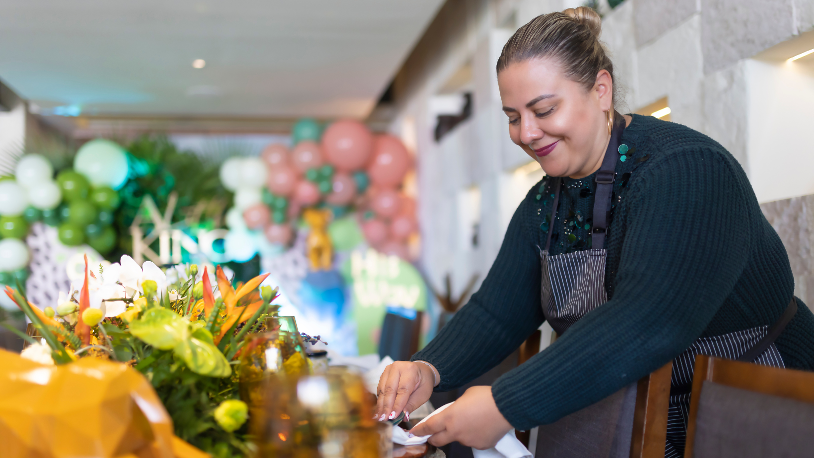 Florist arranging a bouquet at a table, with colorful flowers and pink balloons in the background