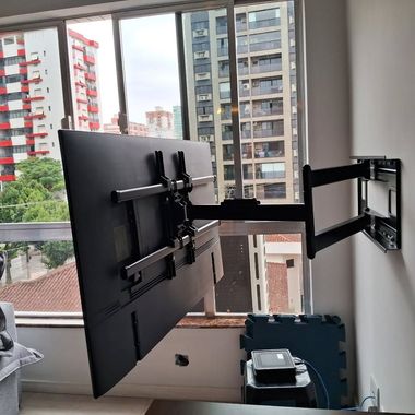 Black monitor mounted on an adjustable wall arm by a window overlooking nearby buildings