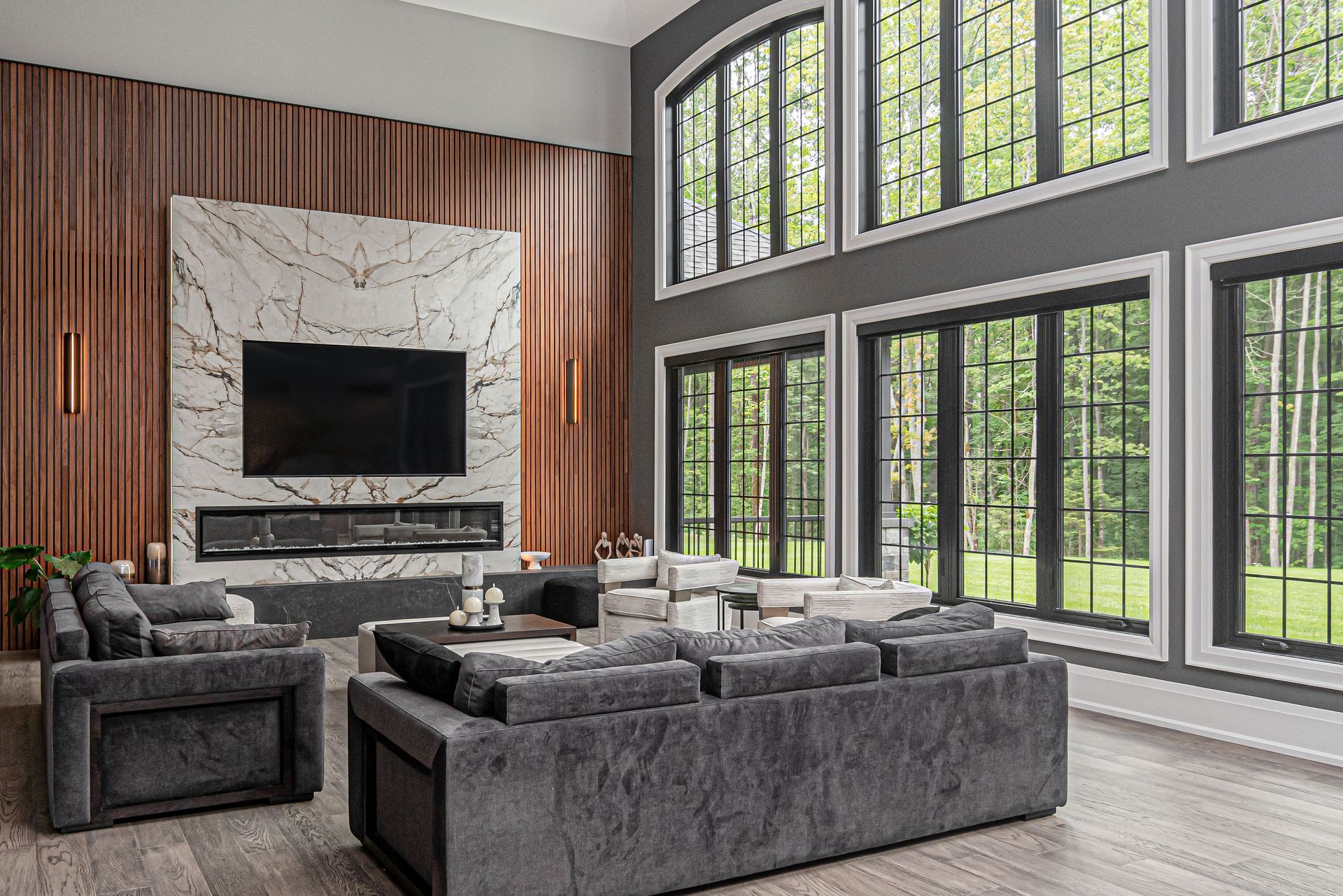 Modern living room with gray sofas, wood accent wall, marble fireplace, and large arched windows
