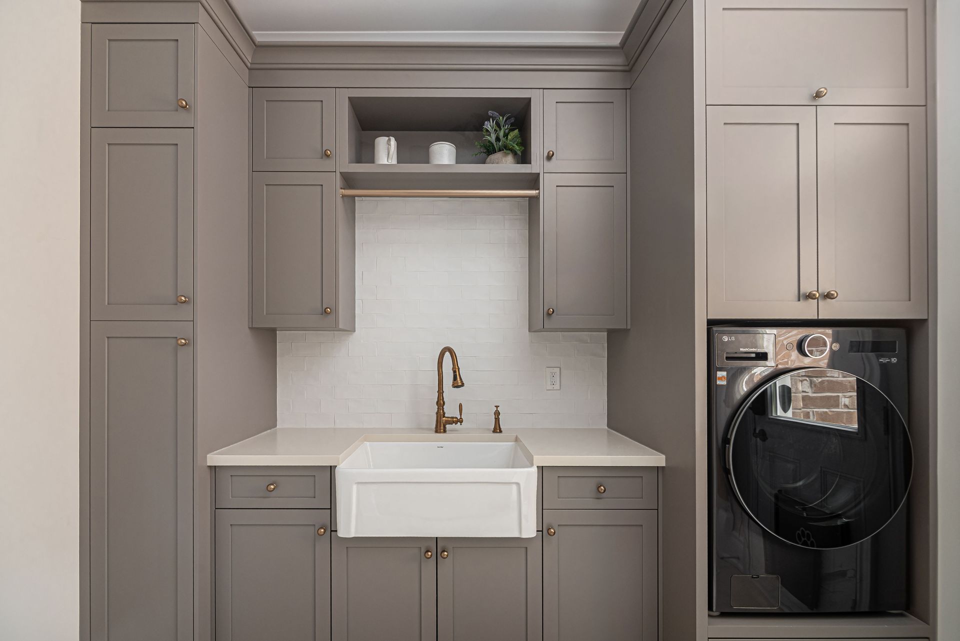 Modern laundry room with gray cabinets, farmhouse sink, and stacked washer-dryer