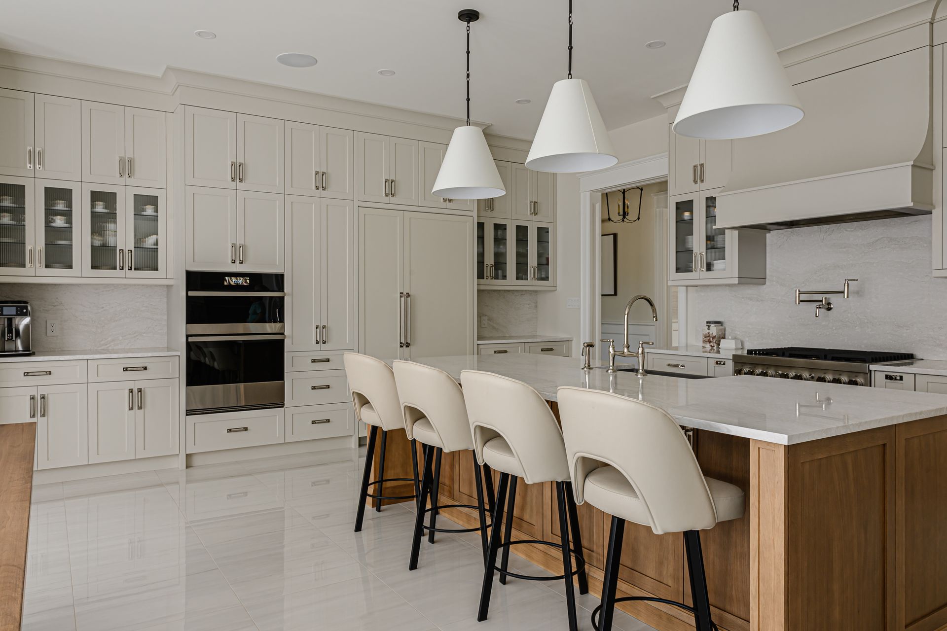 Bright white kitchen with island seating, pendant lights, built-in ovens, and light wood cabinets