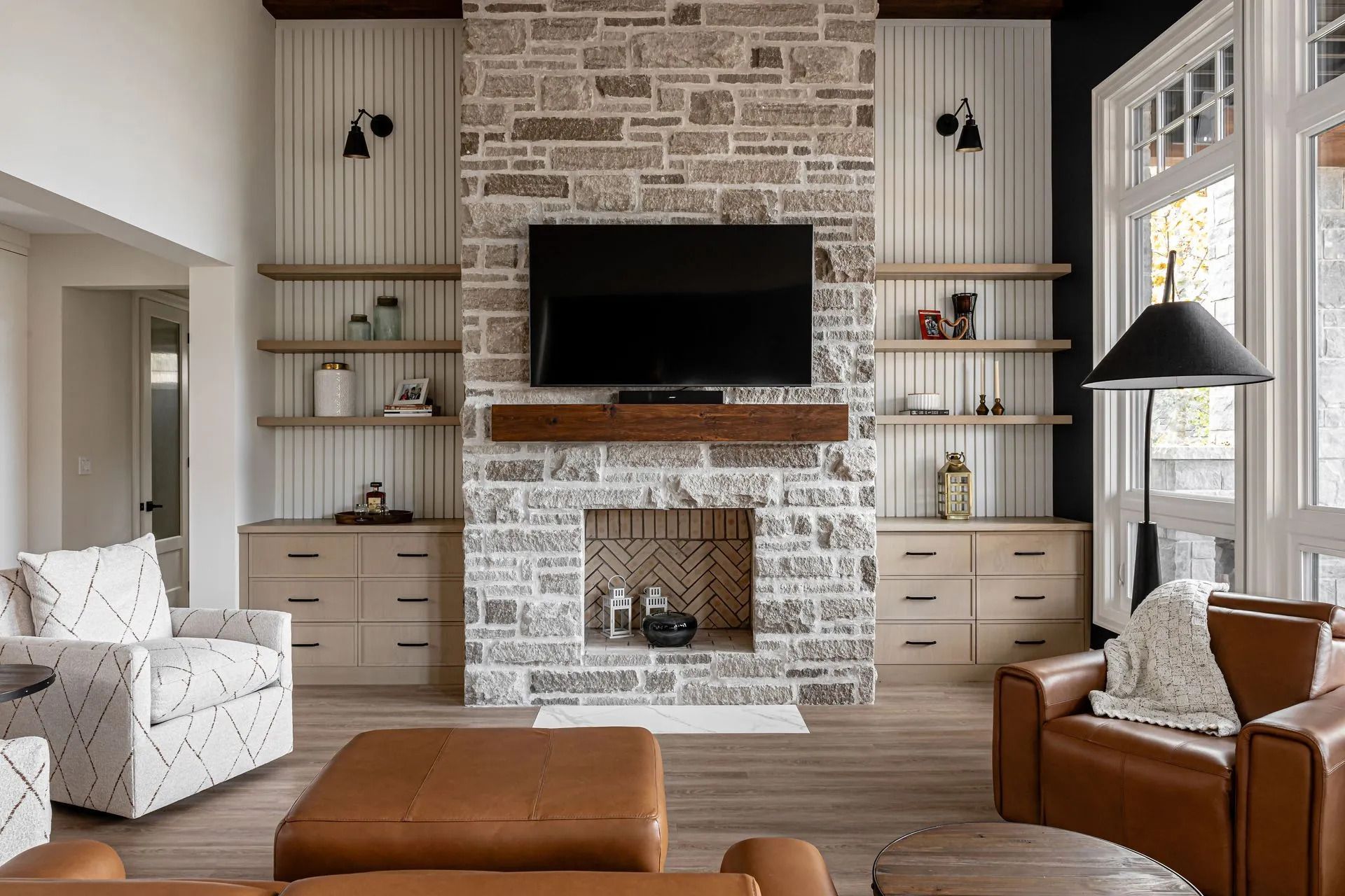 Bright living room with a brick fireplace, wall-mounted TV, built-in shelves, and tan leather seating.