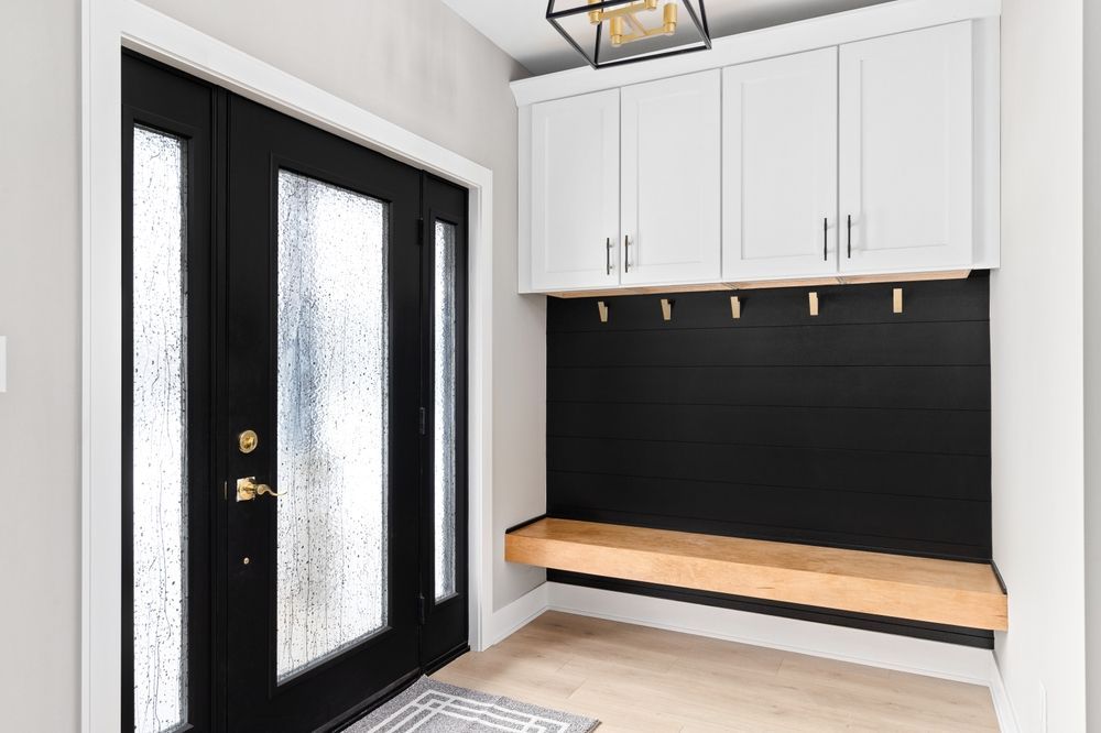 Modern entryway with black double doors, white cabinets, and a wooden bench with hooks above.