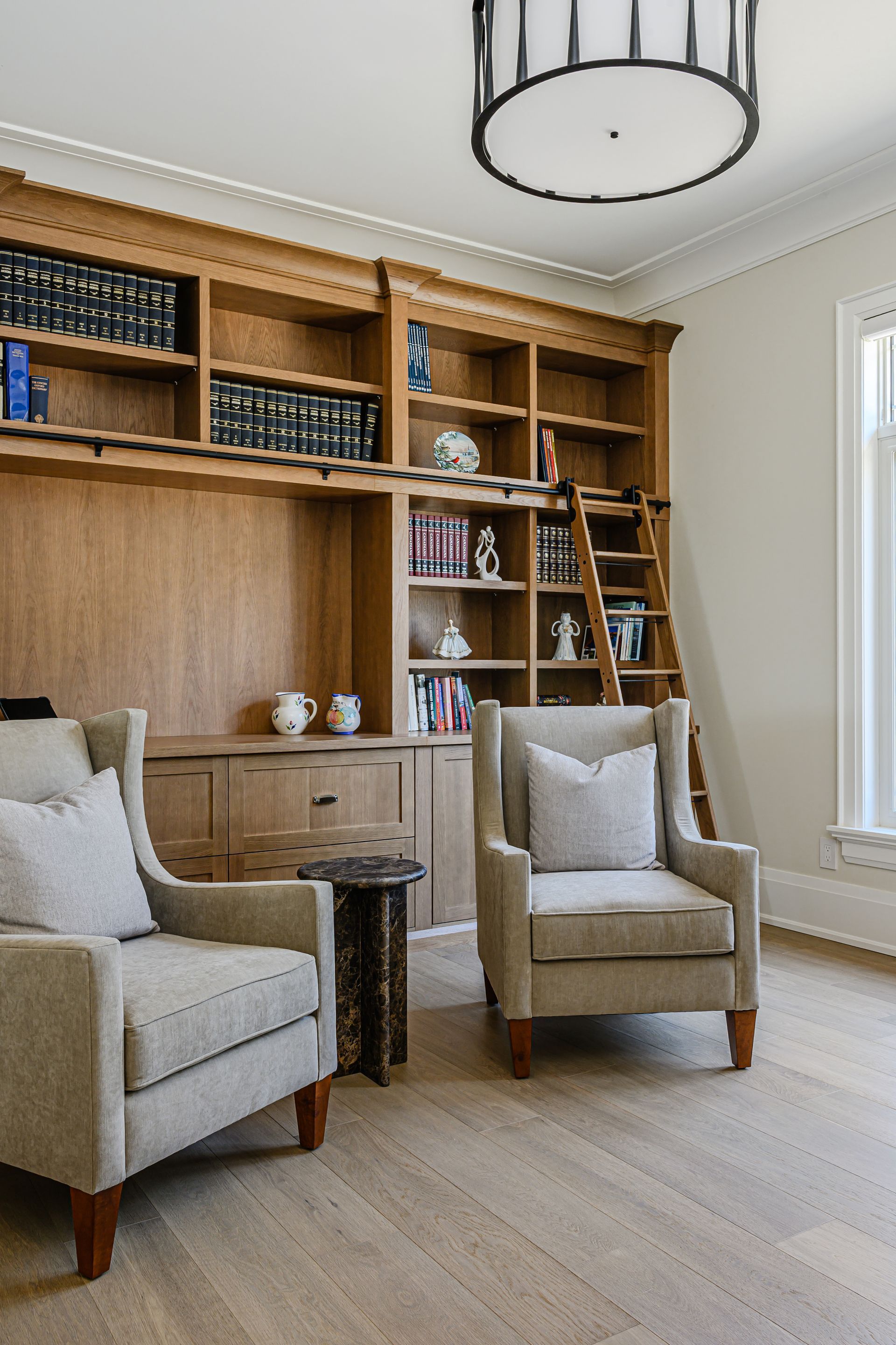 Bright living room with built-in wood shelves, two beige armchairs, and a chandelier