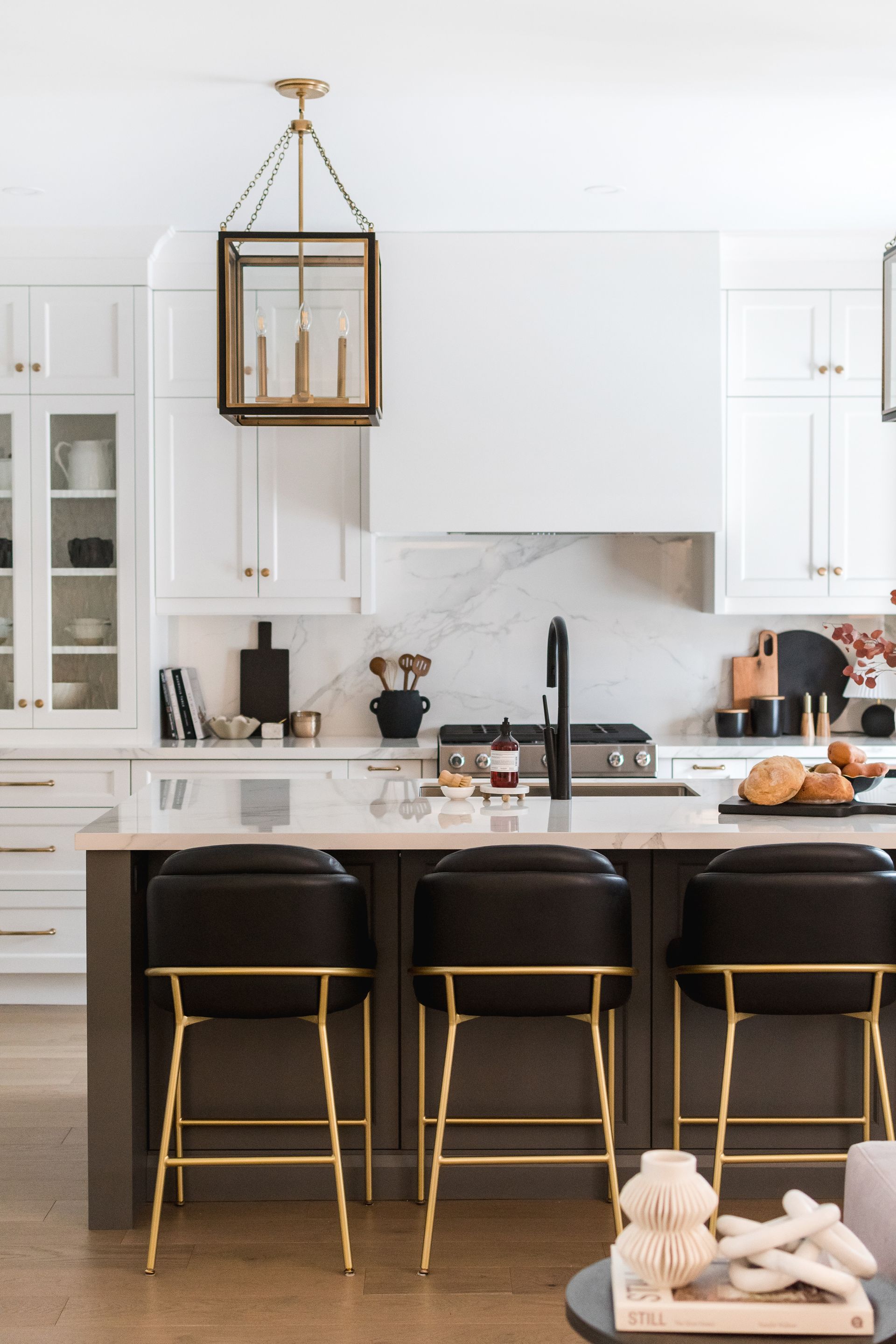 A kitchen with white cabinets , black stools and a large island.