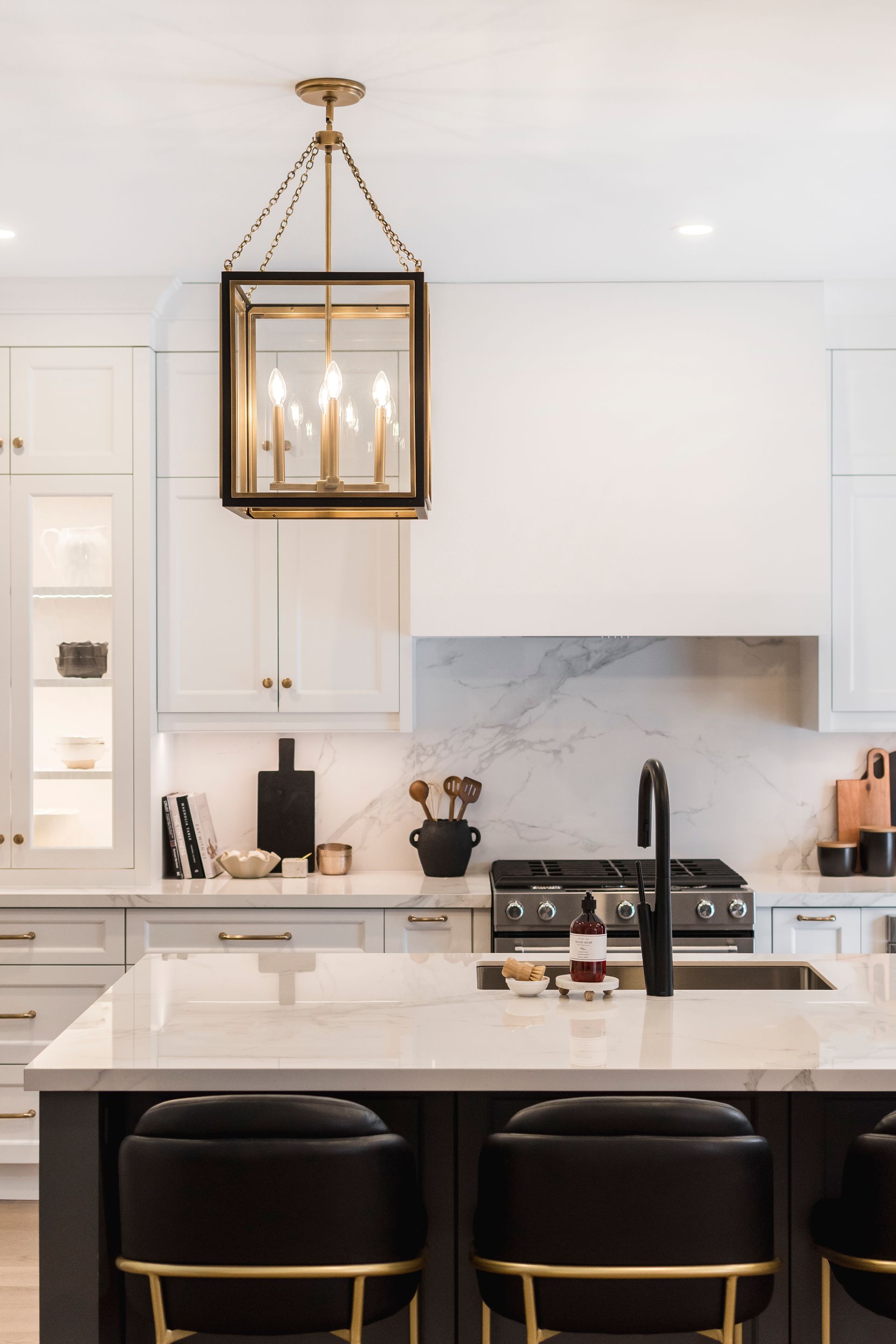 A kitchen with a stove , sink , chairs and a chandelier hanging from the ceiling.