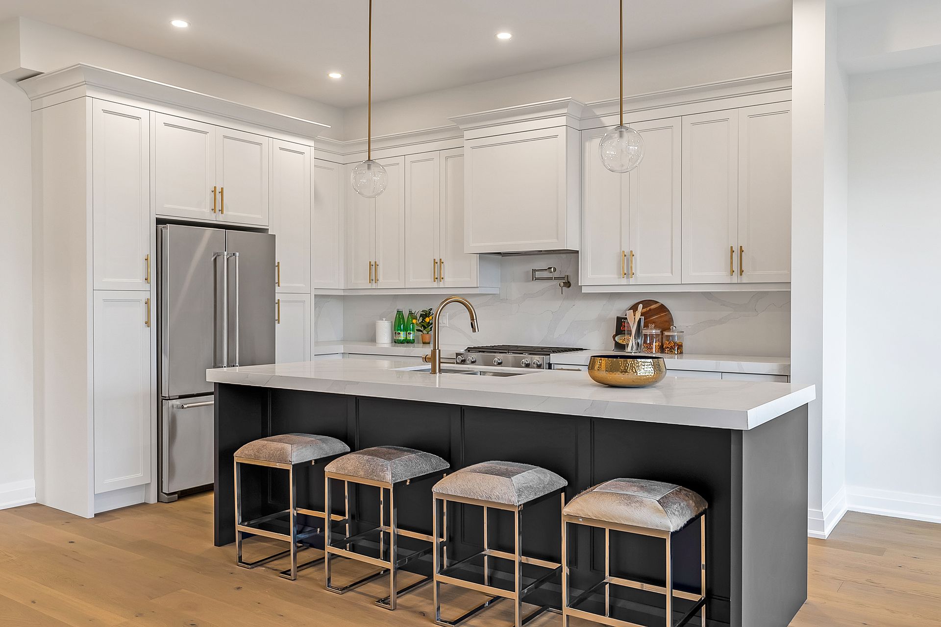A kitchen with white cabinets , a large island , stools and a refrigerator.