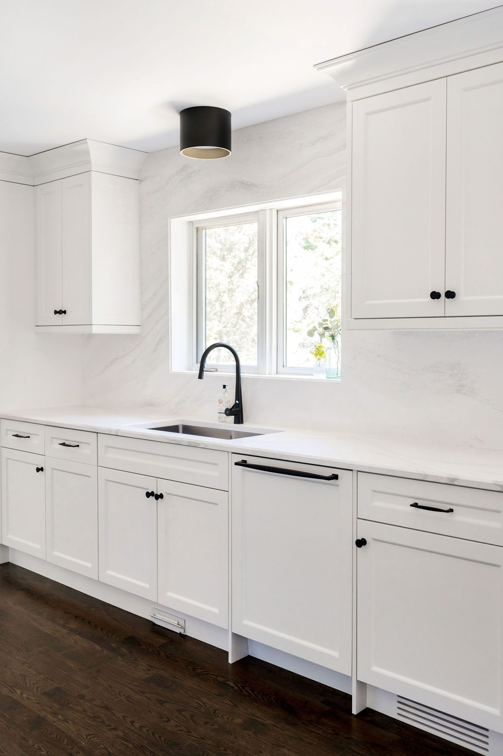 A kitchen with white cabinets , a sink , and a window.