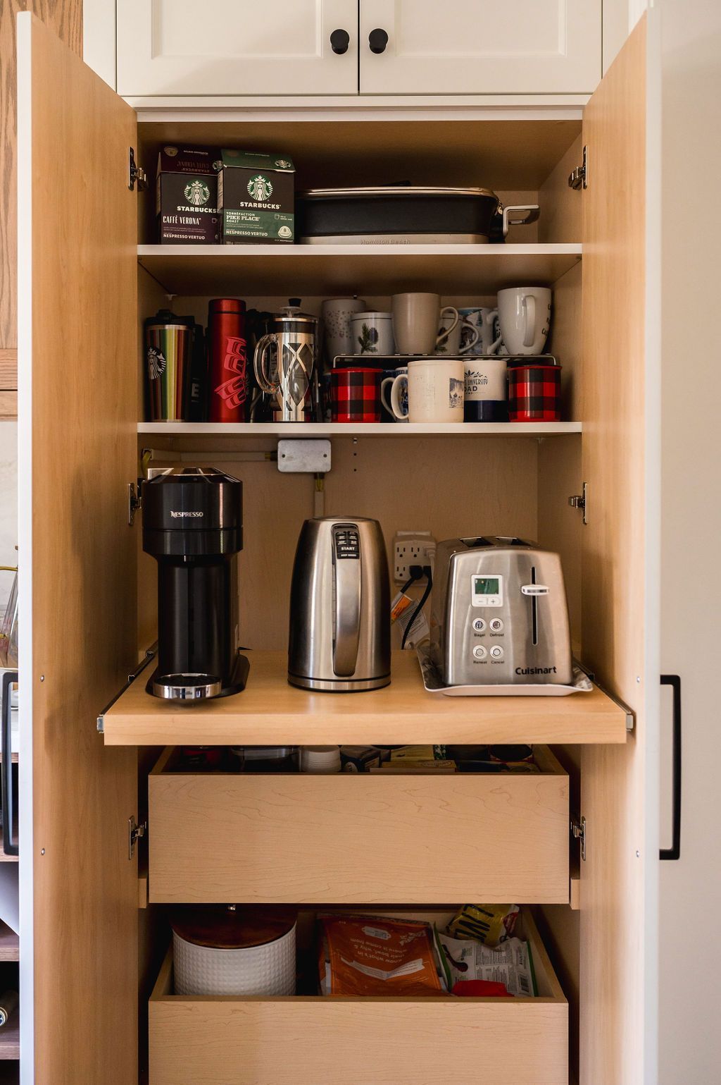 A kitchen cabinet with a coffee maker , kettle , and toaster.