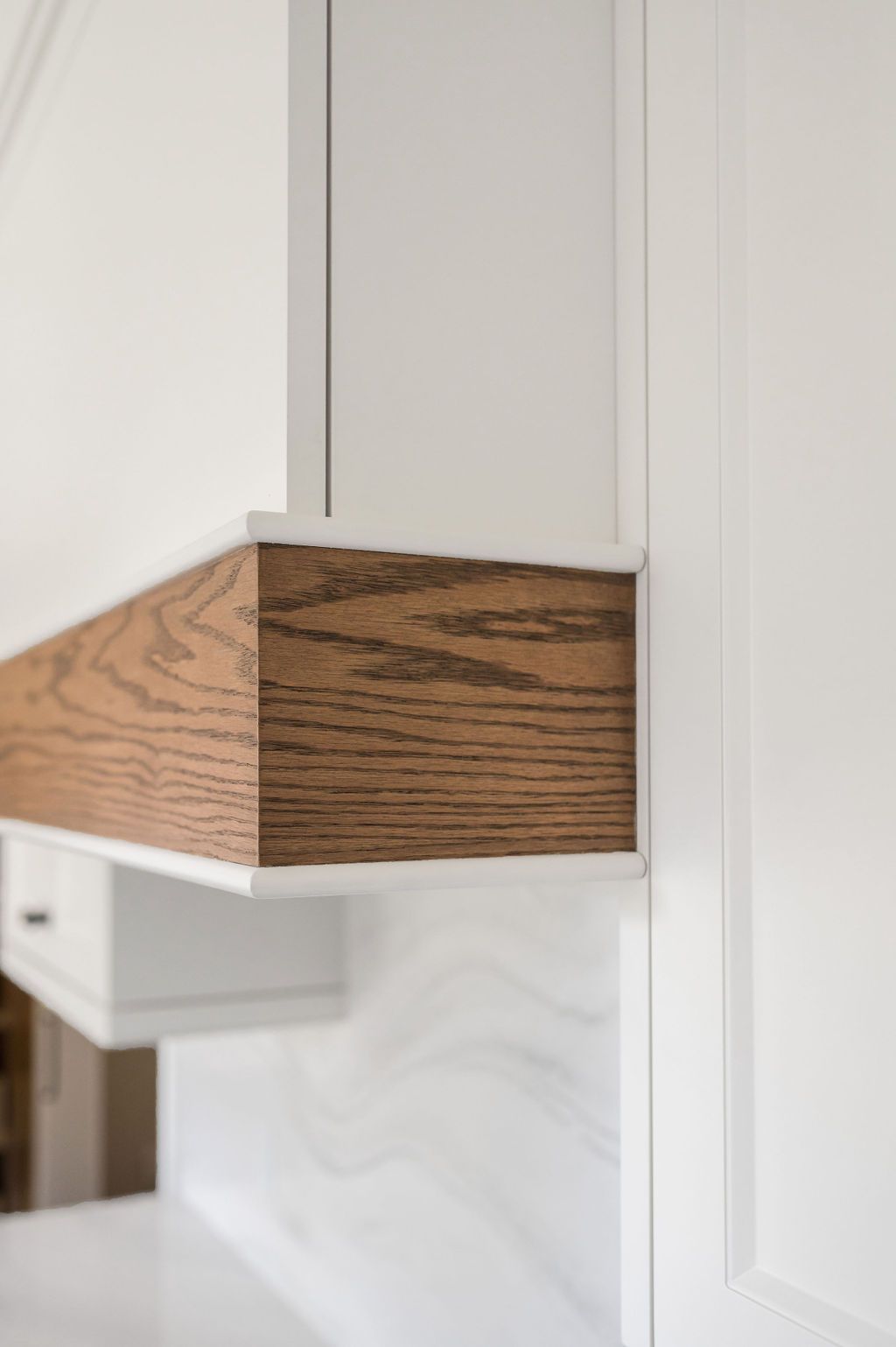 A kitchen with white cabinets and a wooden hood.