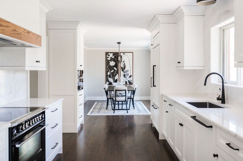 A kitchen with white cabinets and black appliances and a dining room in the background.