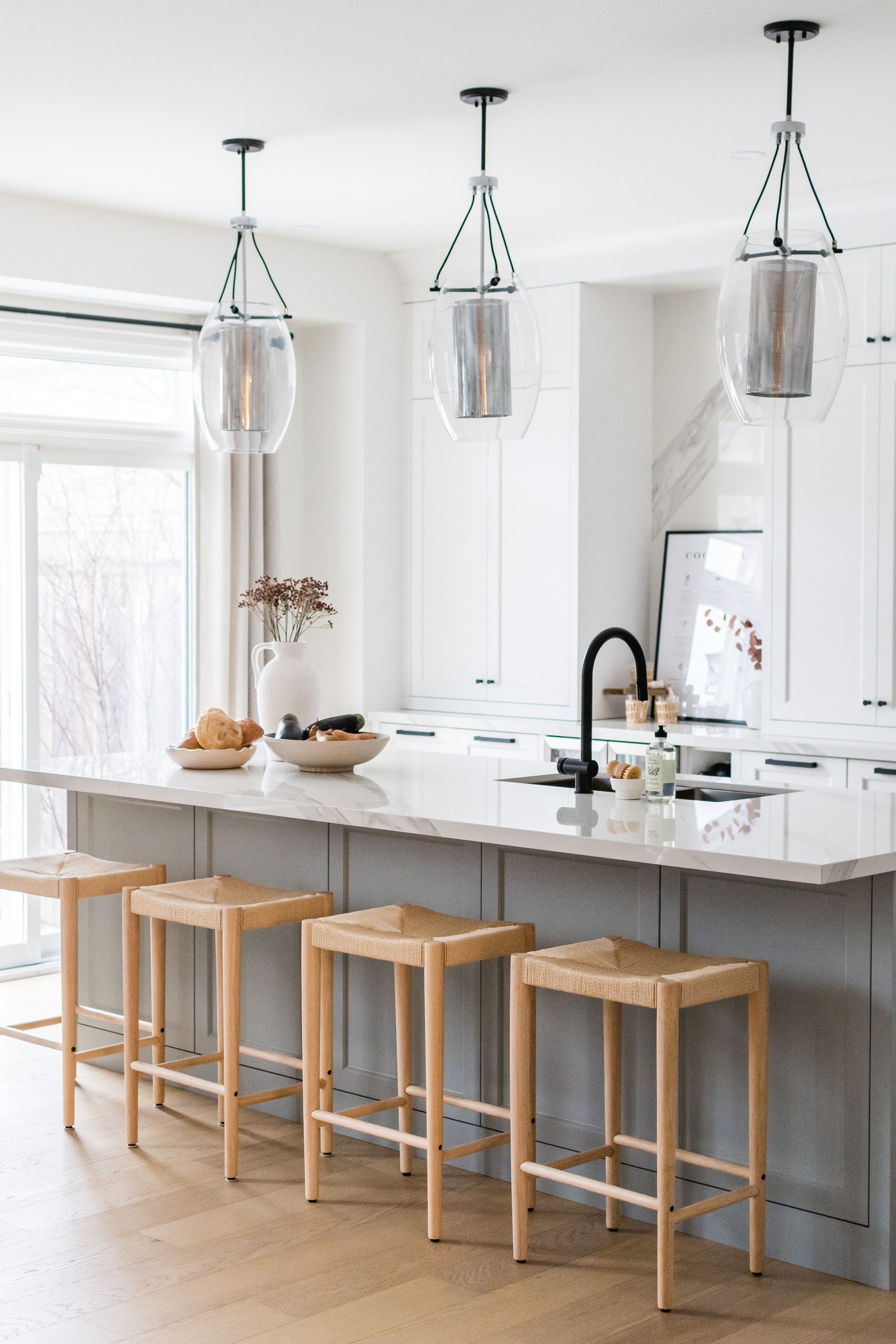 A kitchen with a large island , stools and pendant lights.