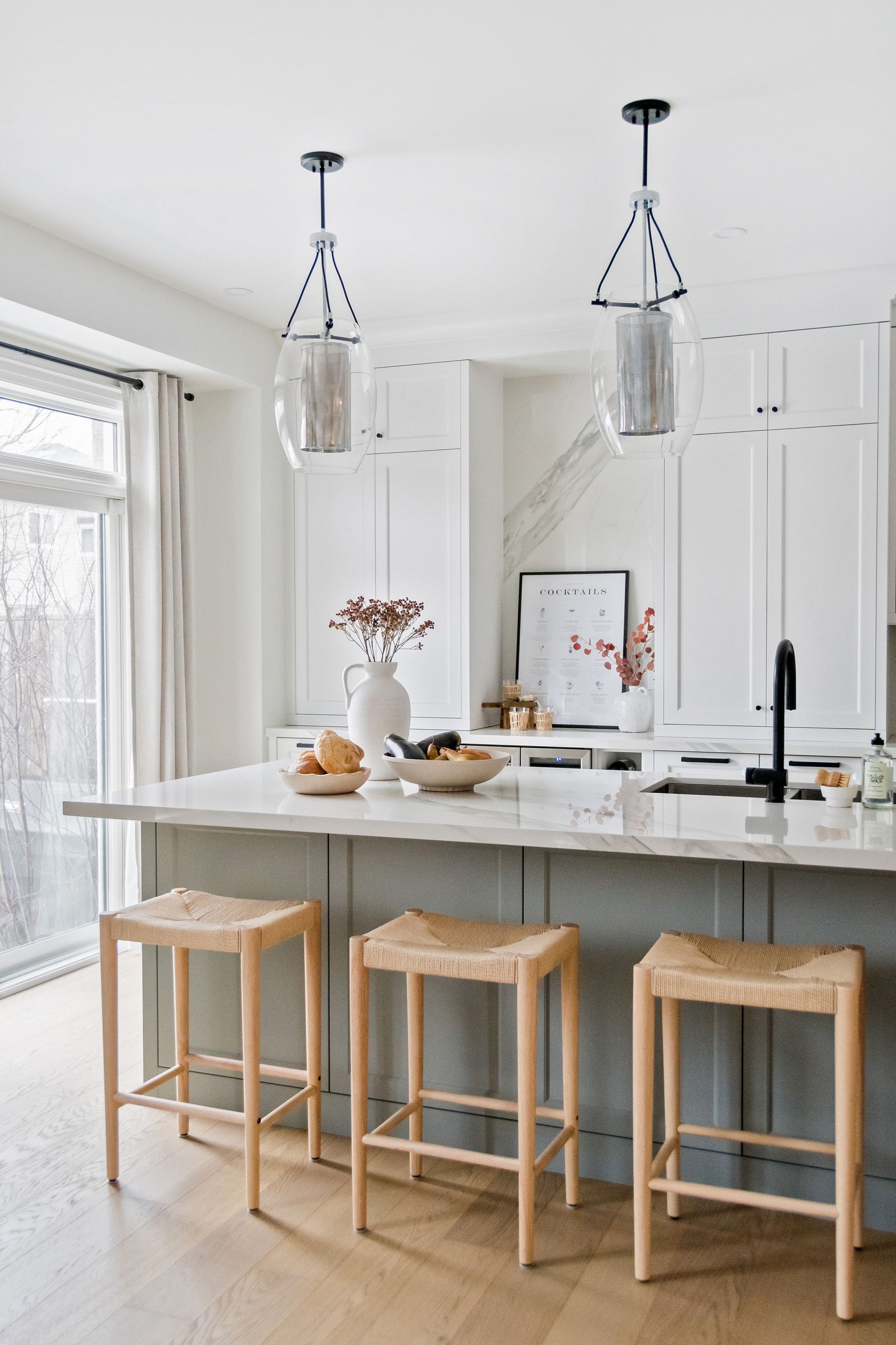 A kitchen with a large island and three wicker stools.