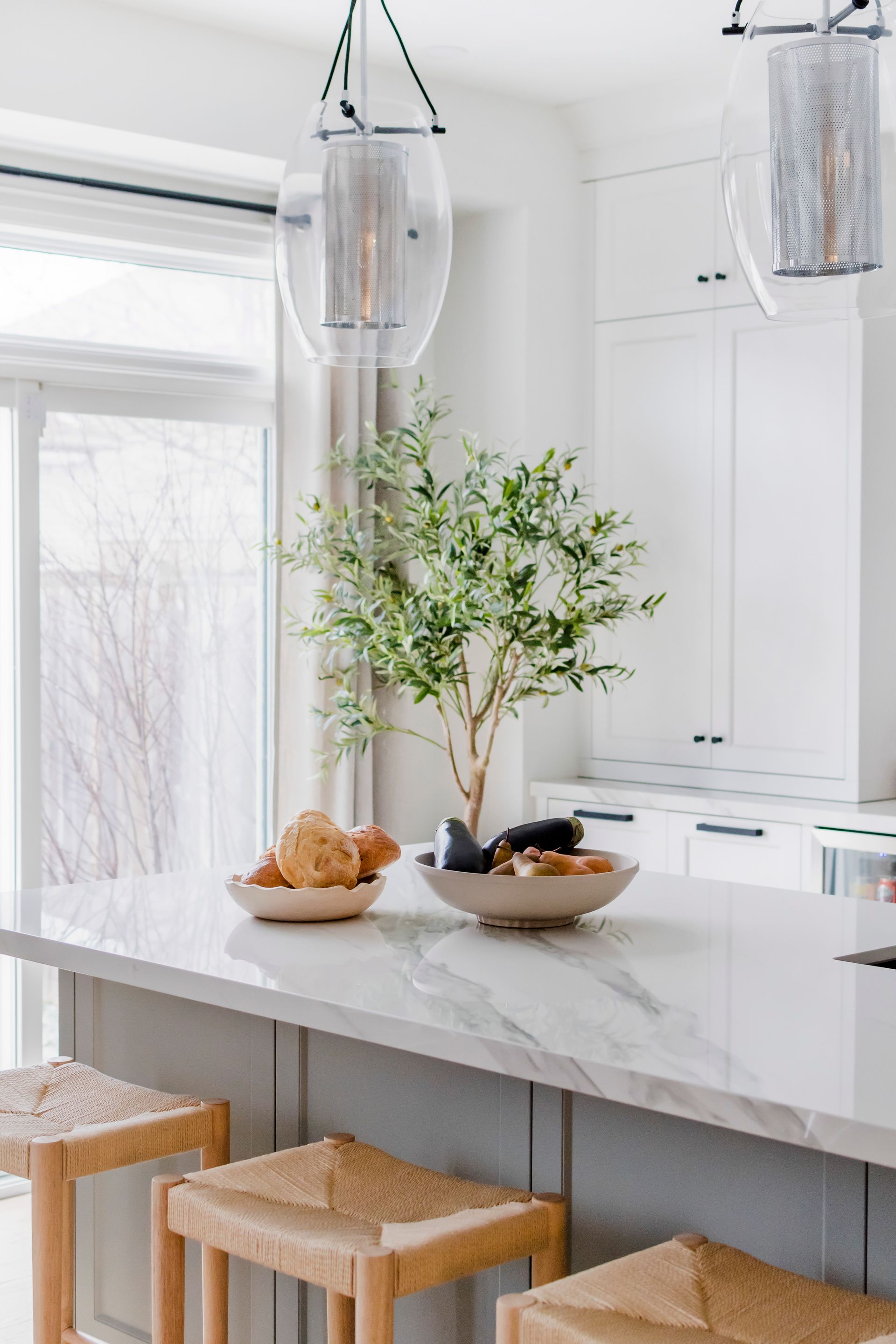 A kitchen with a marble counter top , wicker stools , and a tree on the counter.