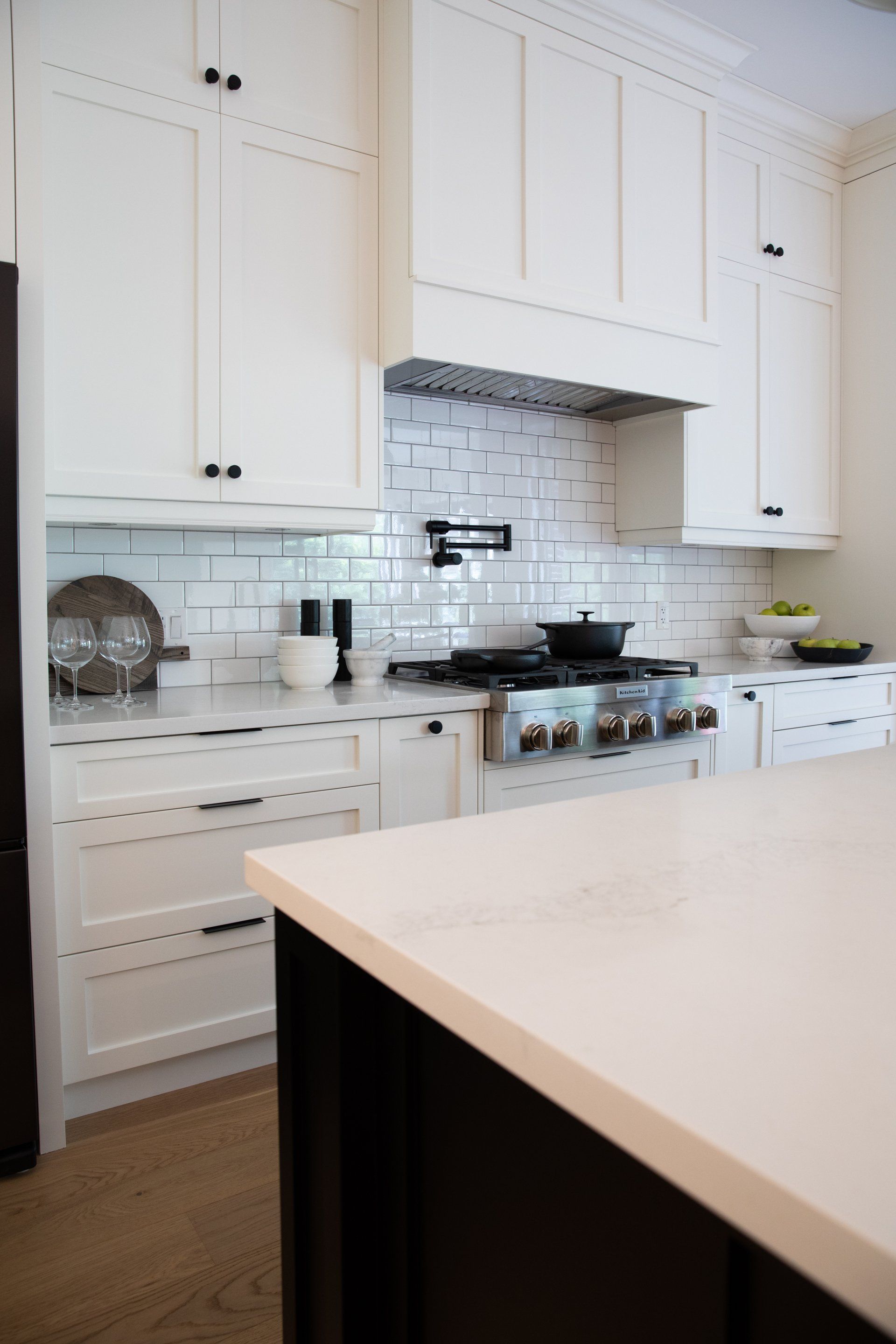 A kitchen with white cabinets , black counter tops , a stove and a refrigerator.