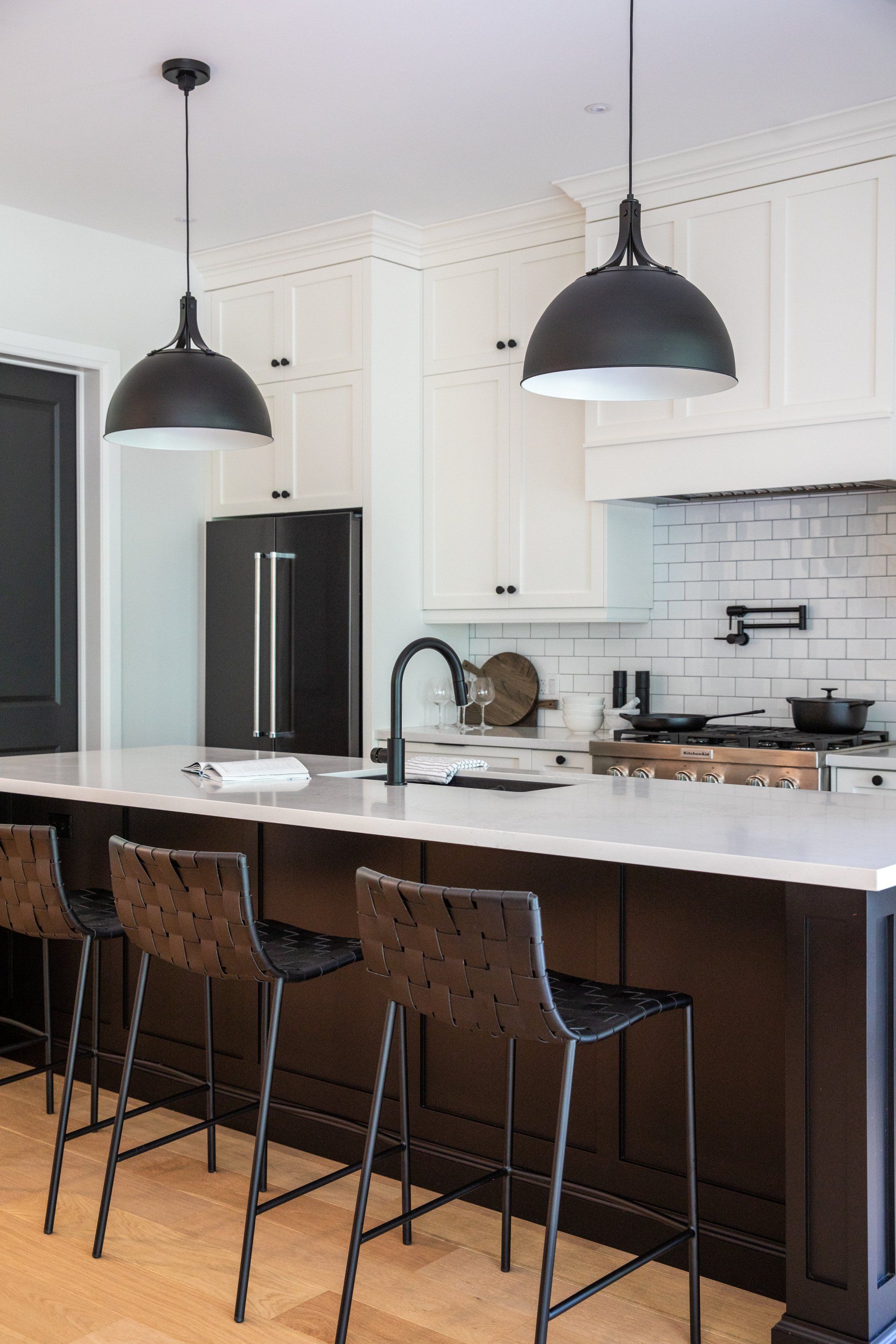 A kitchen with a long island , stools , a refrigerator and a sink.