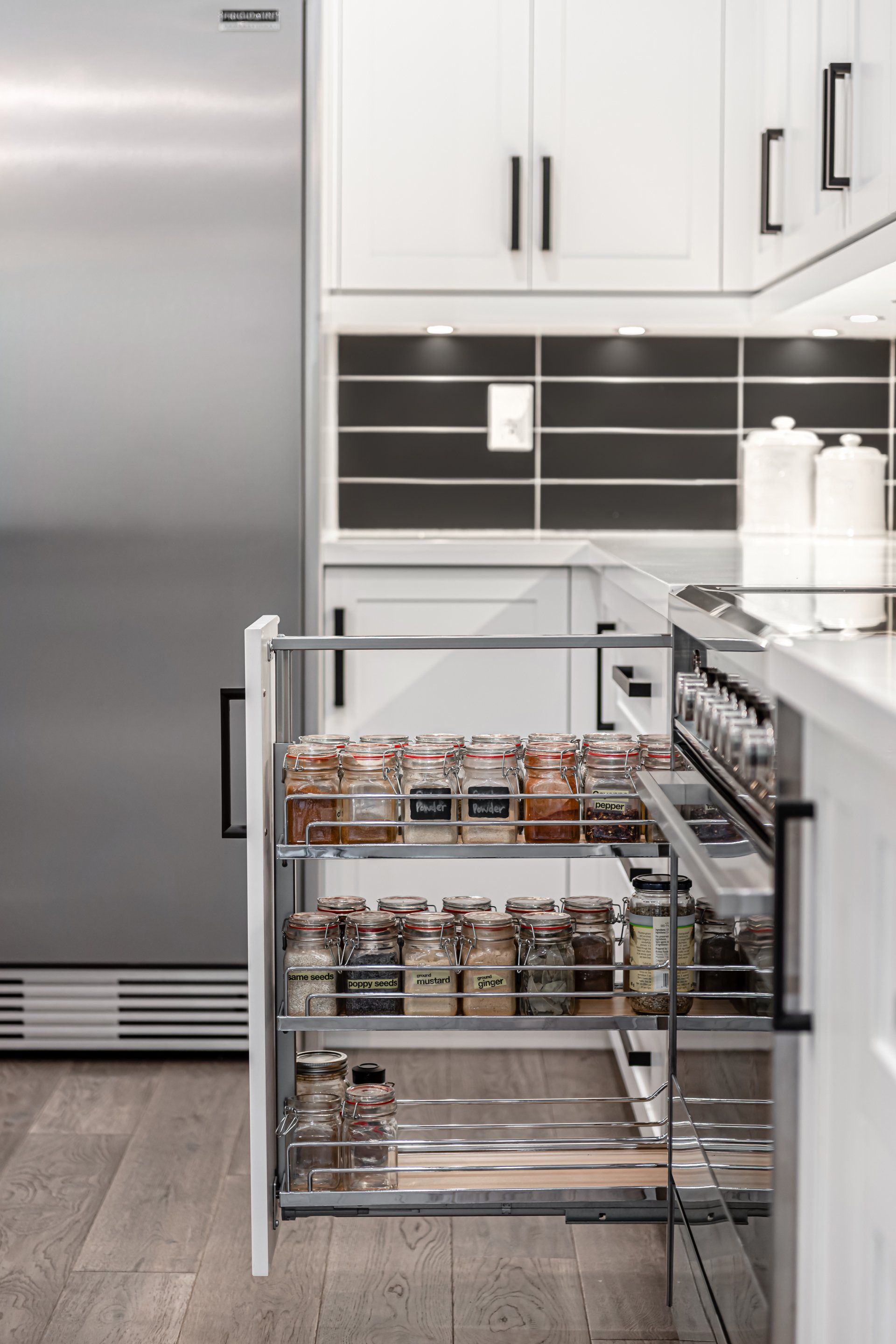 A kitchen with white cabinets and stainless steel appliances and a pull out drawer filled with spices.