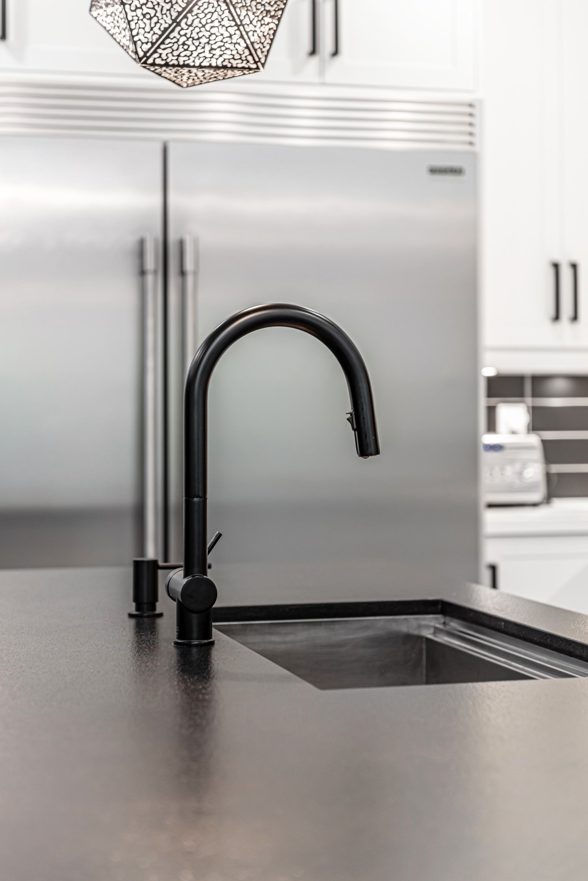 A kitchen sink with a black faucet and a stainless steel refrigerator.