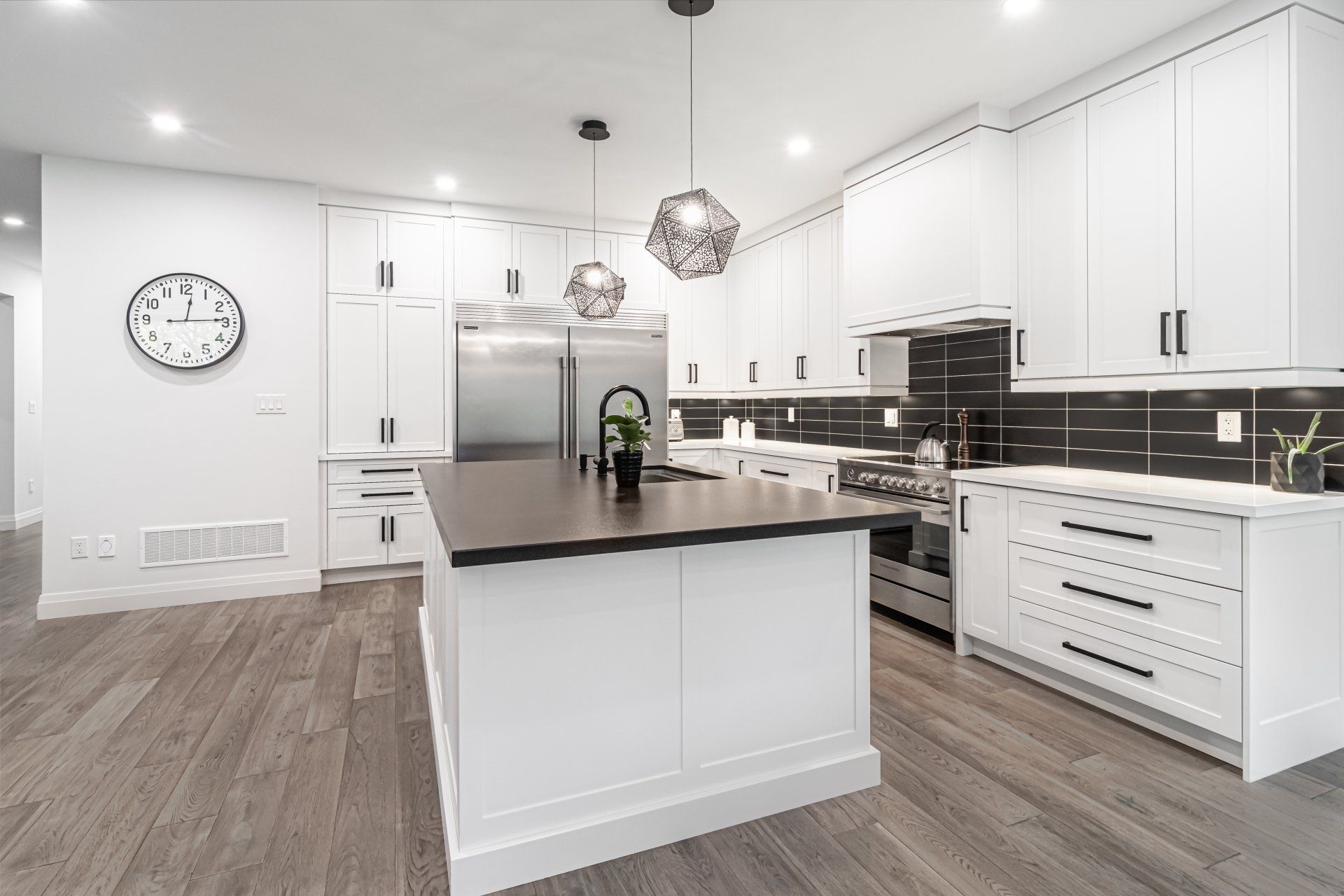 A kitchen with white cabinets , stainless steel appliances , a large island and a clock on the wall.