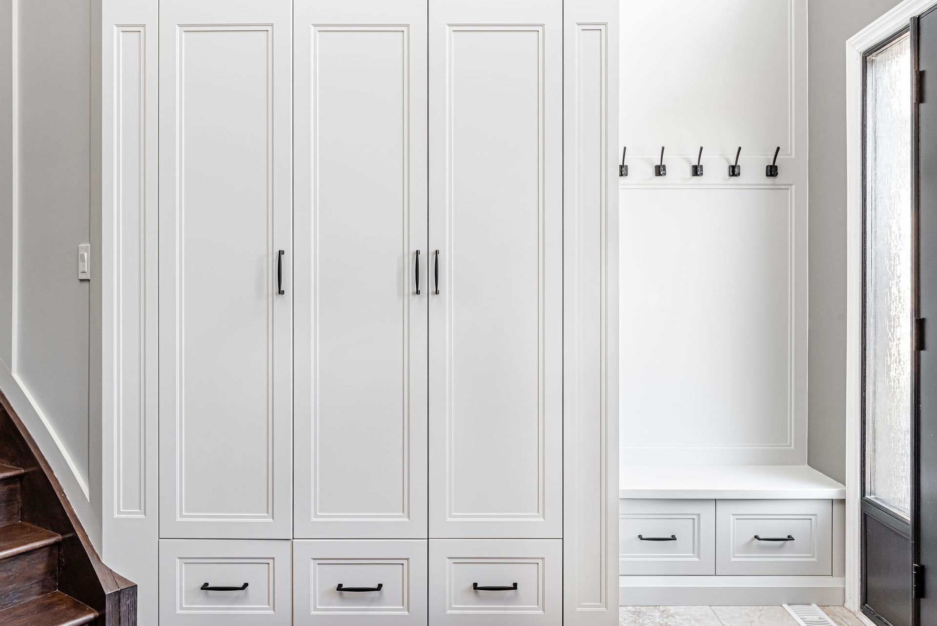 A hallway with white cabinets , drawers , and a bench.