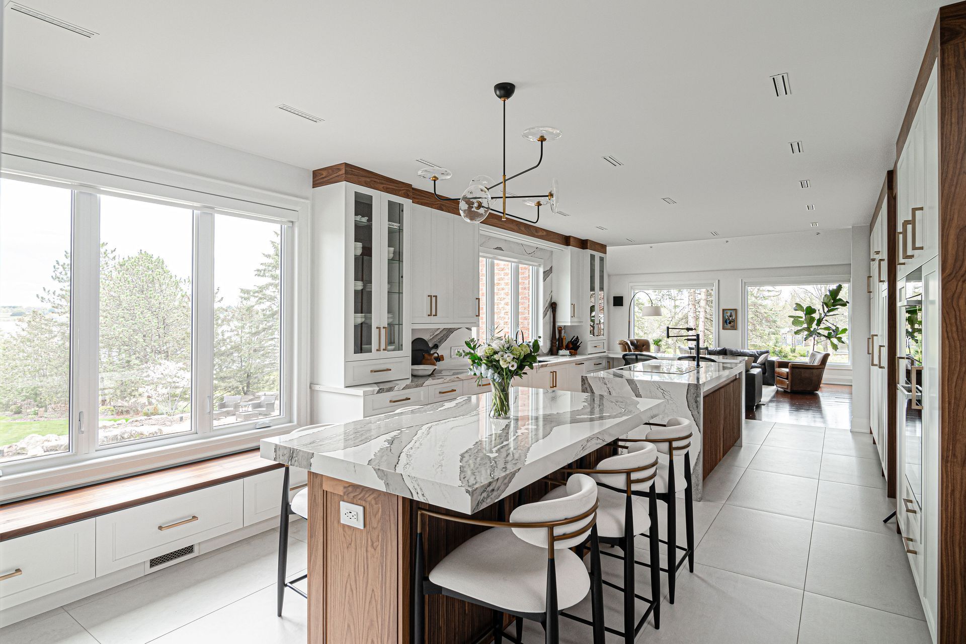 A kitchen with white cabinets , marble counter tops , stools and a large island.
