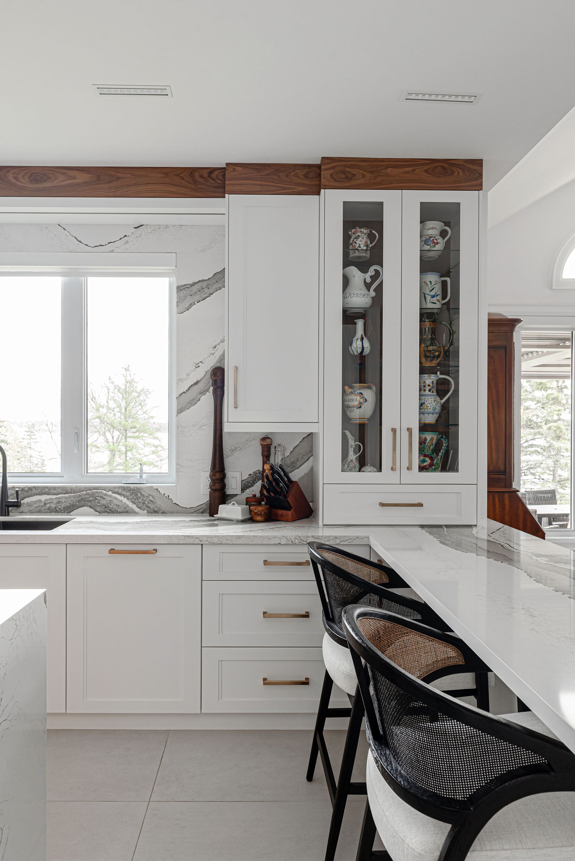 A kitchen with white cabinets and stools and a window.