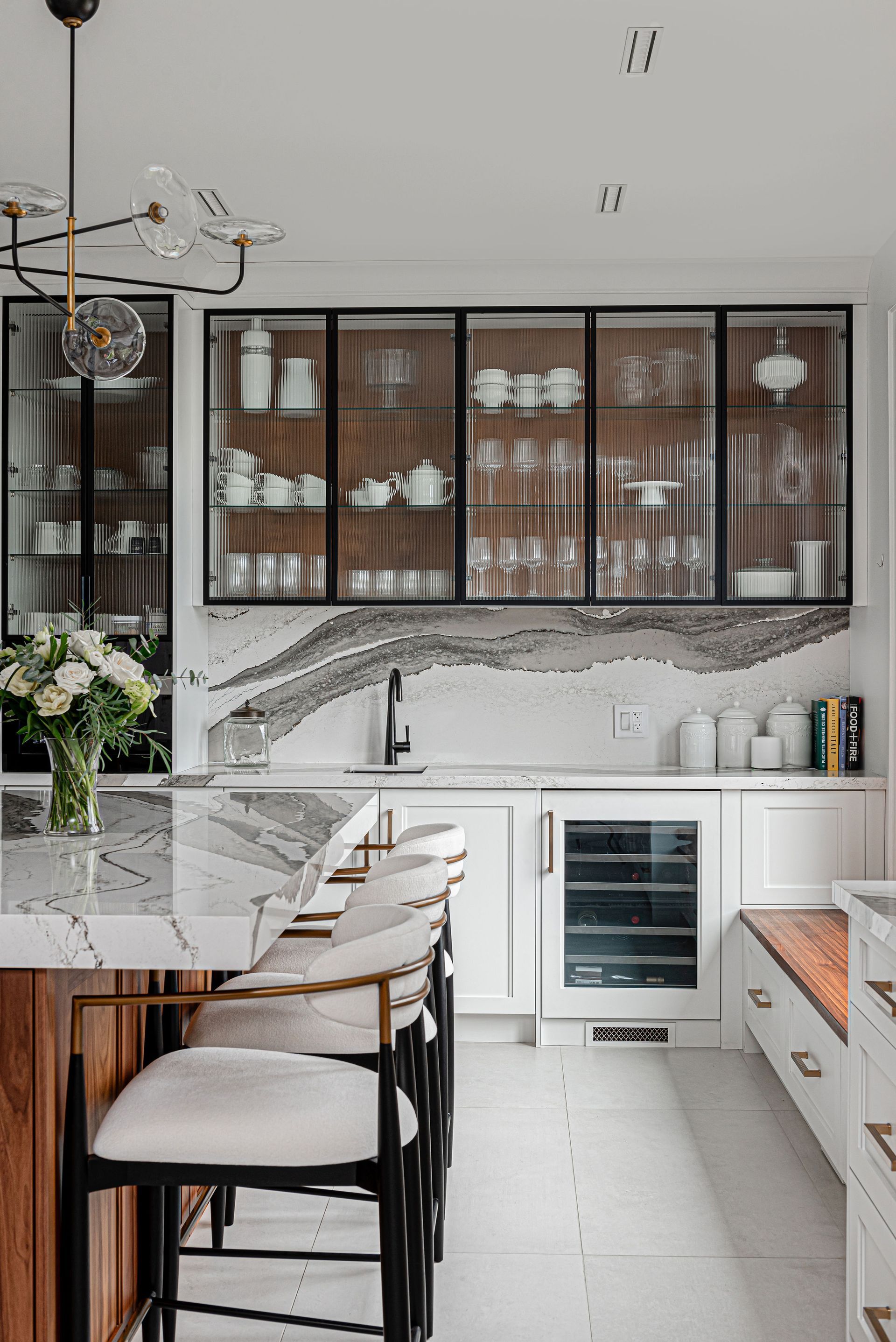 A kitchen with a marble counter top , stools , and a refrigerator.