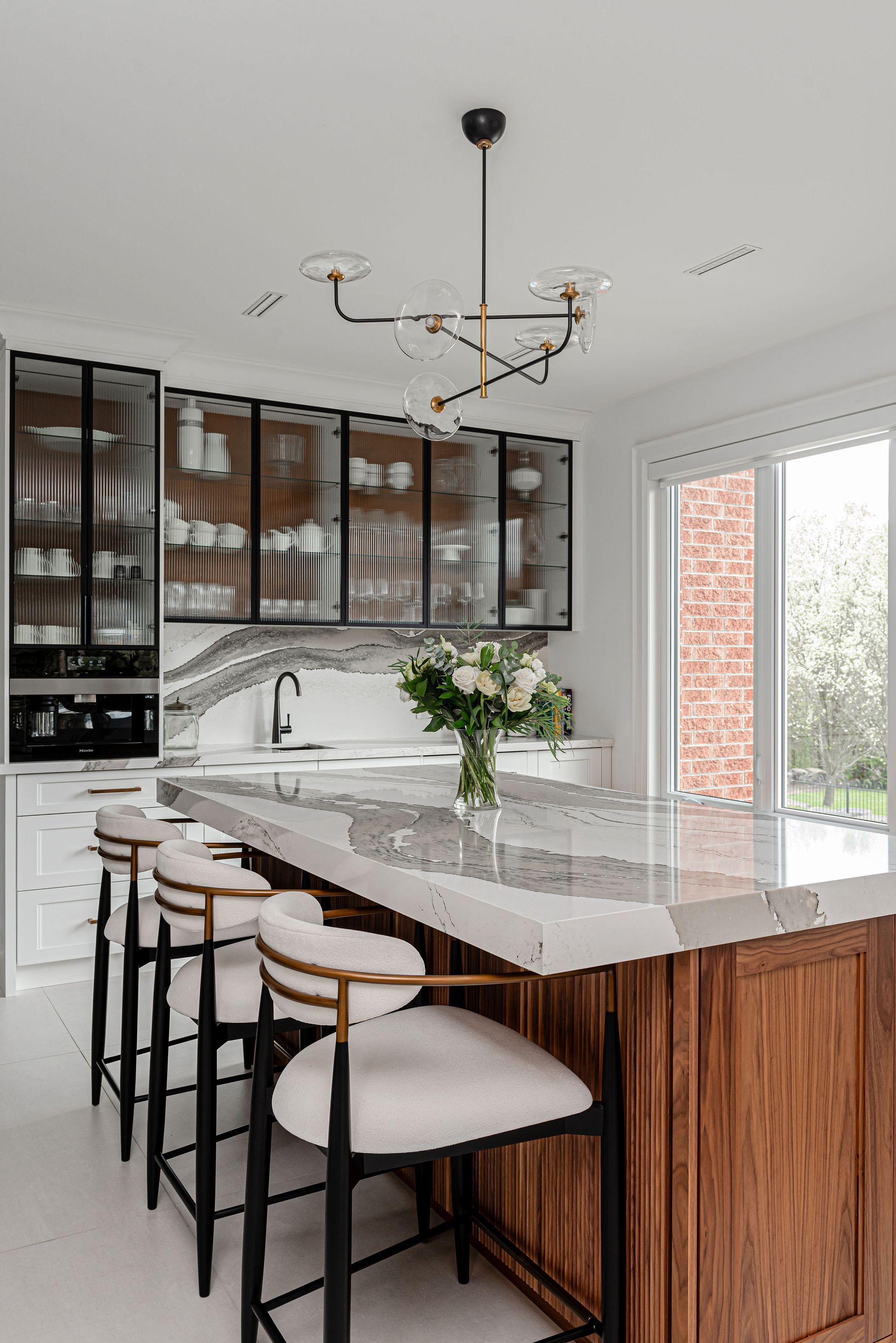 A kitchen with a large island , stools and a chandelier.