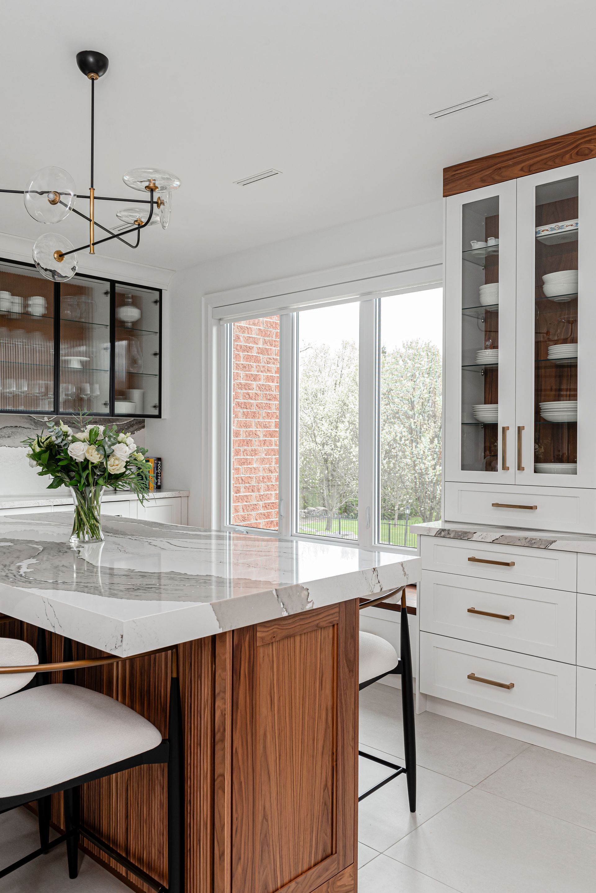 A kitchen with a large island , white cabinets , and a vase of flowers on the counter.