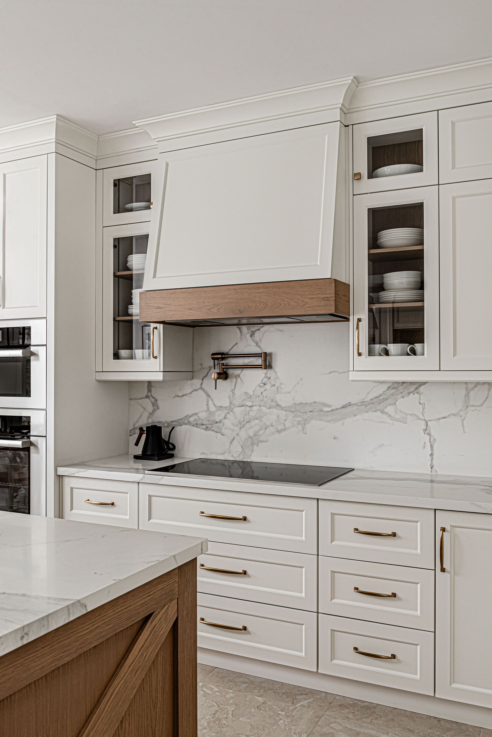 A kitchen with white cabinets and a wooden hood.
