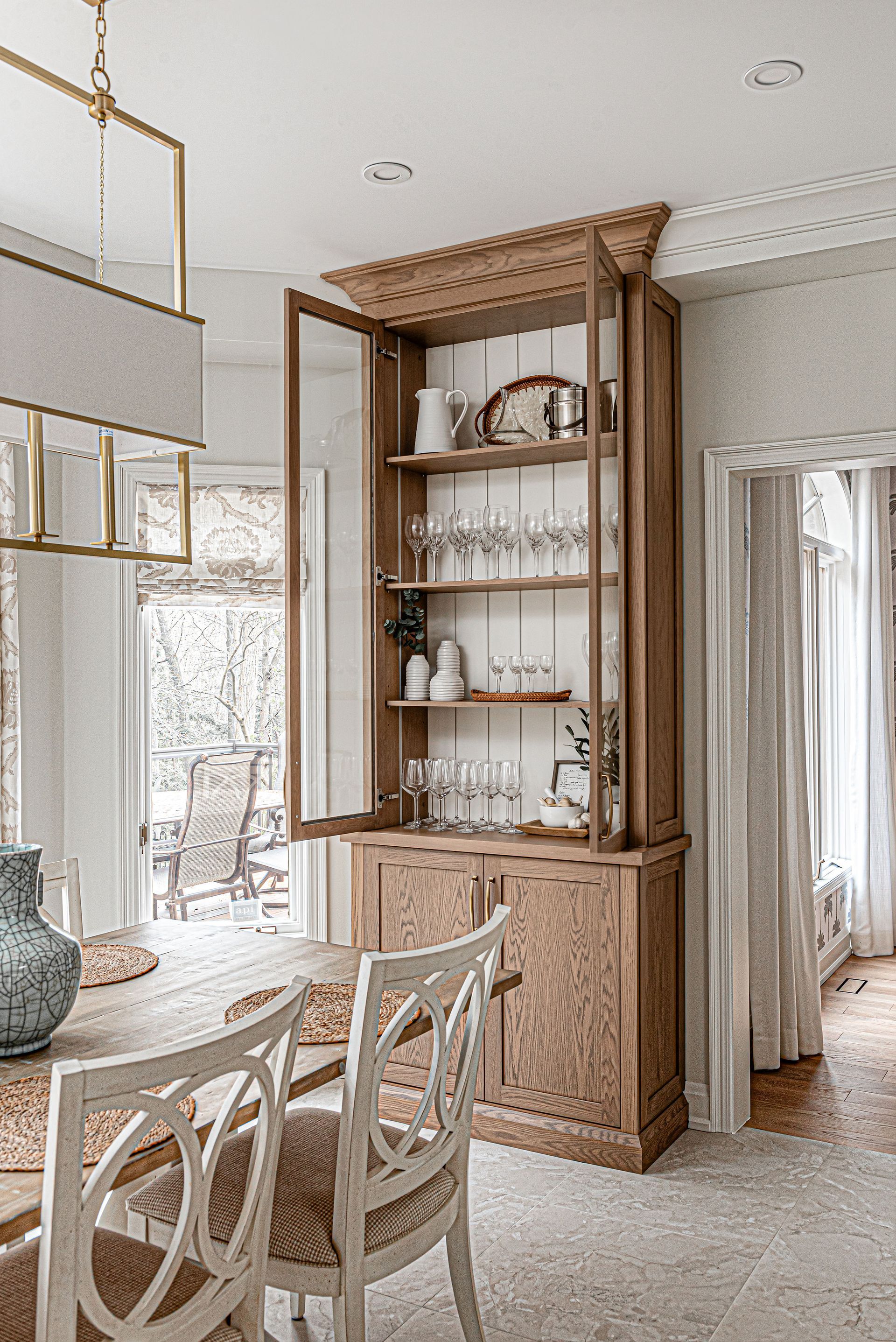 A dining room with a table and chairs and a hutch with the doors open.