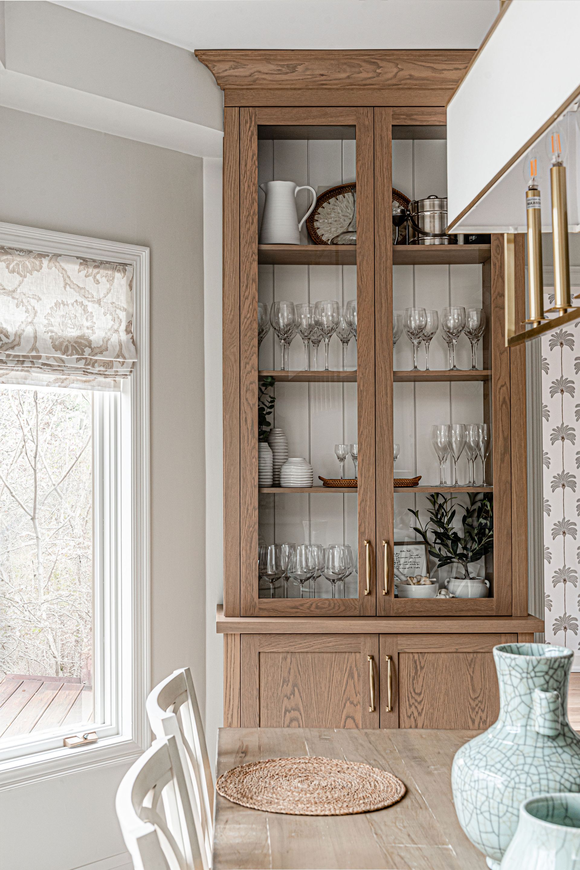 A dining room with a glass cabinet filled with wine glasses and plates.