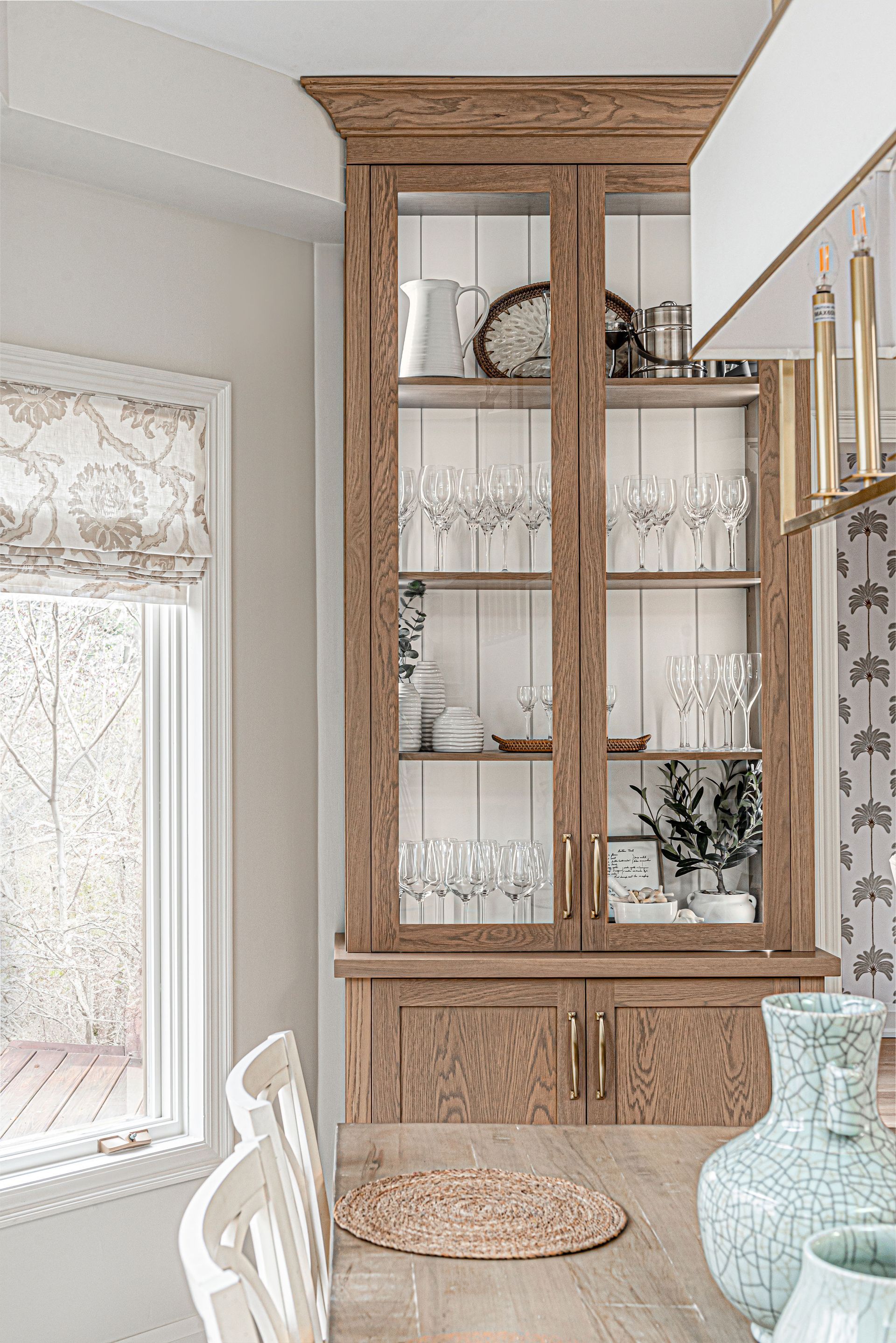 A dining room with a hutch filled with plates , glasses , and vases.