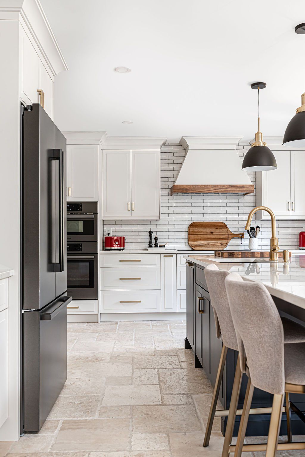 A kitchen with white cabinets , a black refrigerator , a sink , and stools.