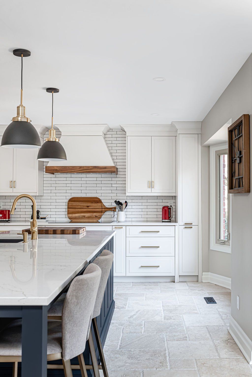 A kitchen with white cabinets , a large island , stools and a clock on the wall.