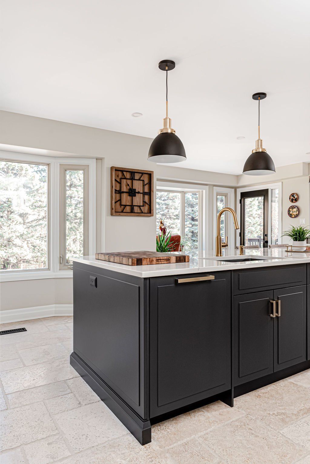 A kitchen with black cabinets , a large island , a sink , and a clock on the wall.